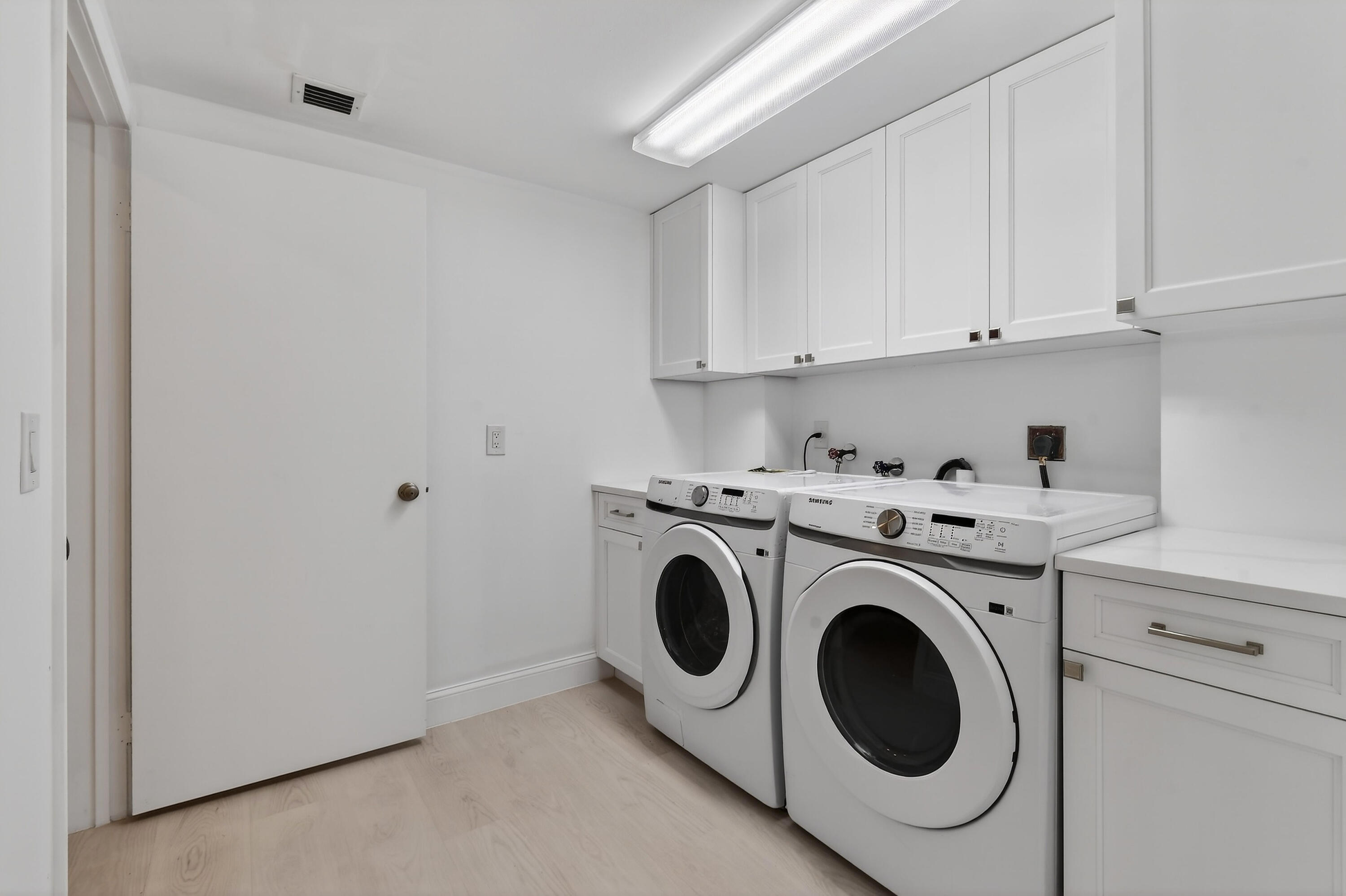 Laundry room with front-loading washer and dryer beneath white cabinets.