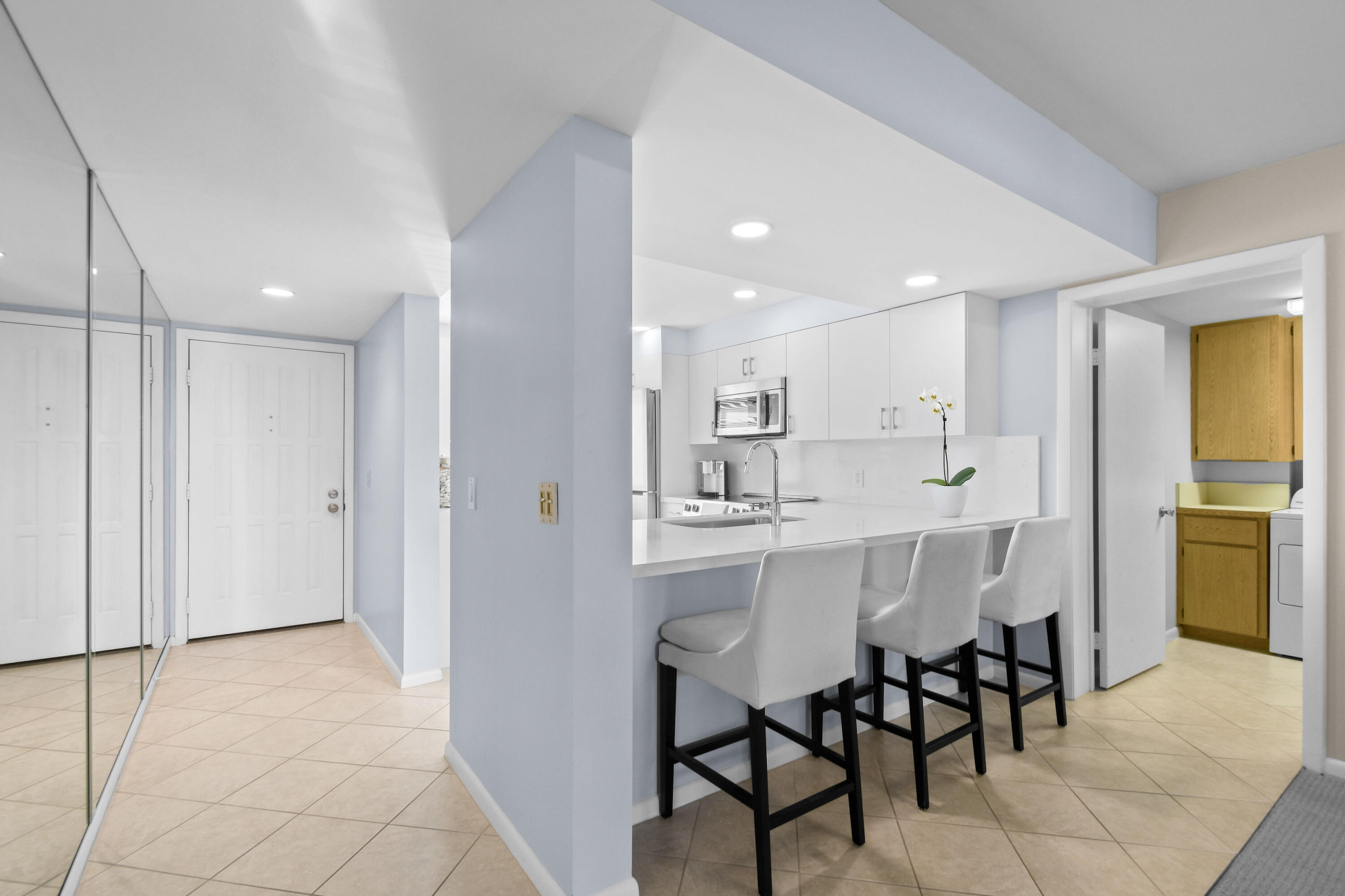 Condo kitchen with a white breakfast bar, three stools, mirrored entry closet, and laundry nook.