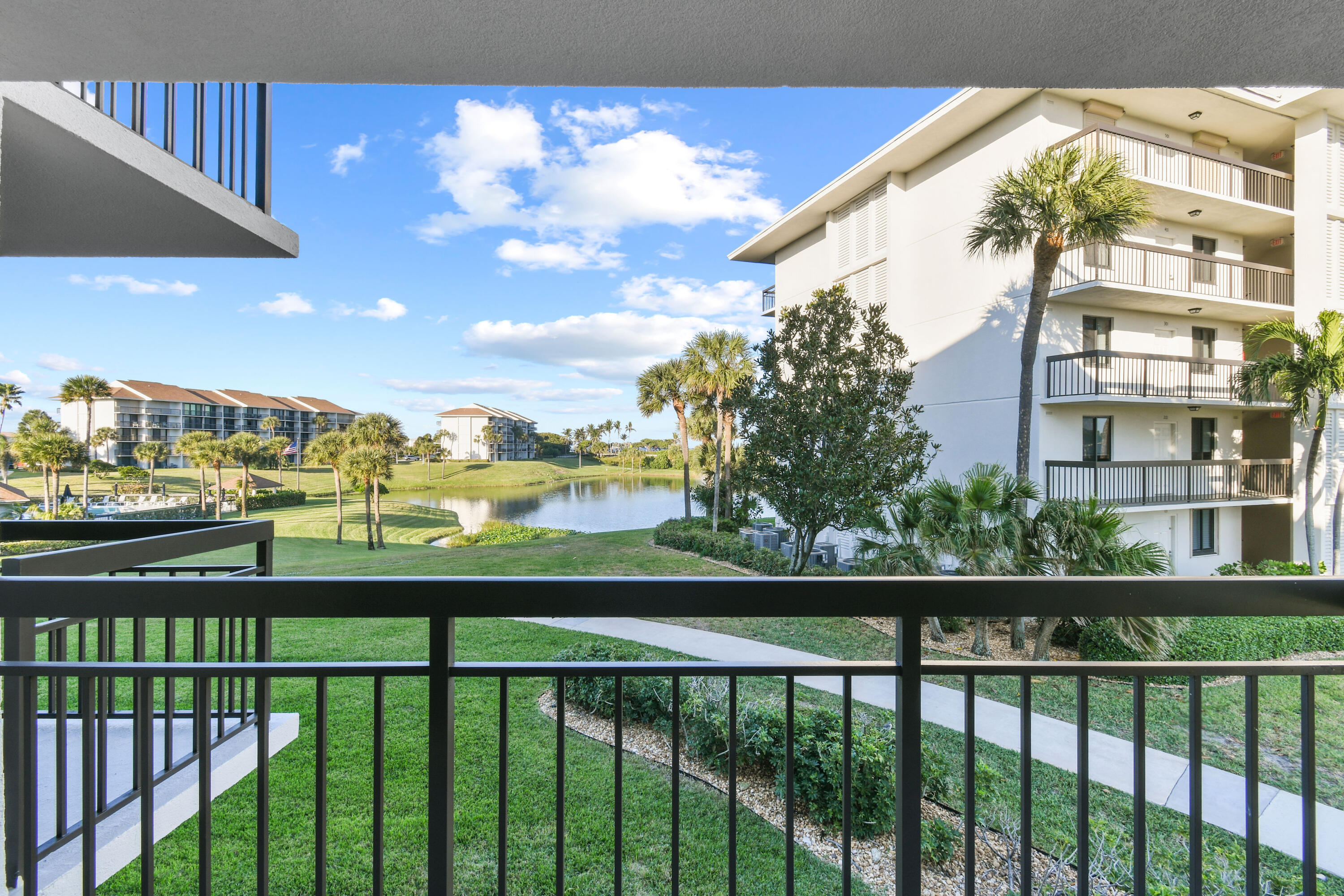 Condominium balcony overlooks a pond, landscaped grounds, and neighboring buildings.