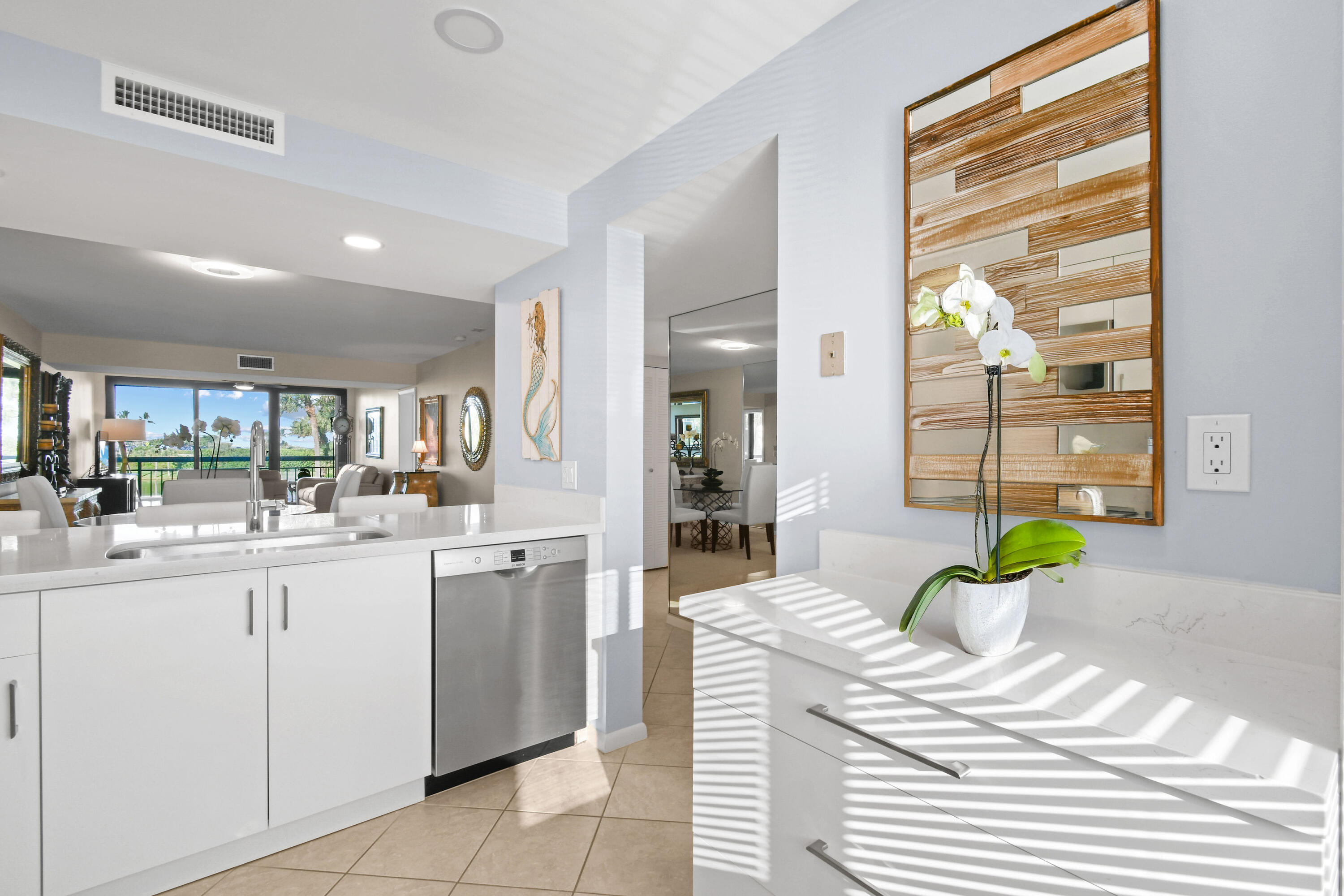 Bright white condo kitchen opening to a living area with balcony and water views.