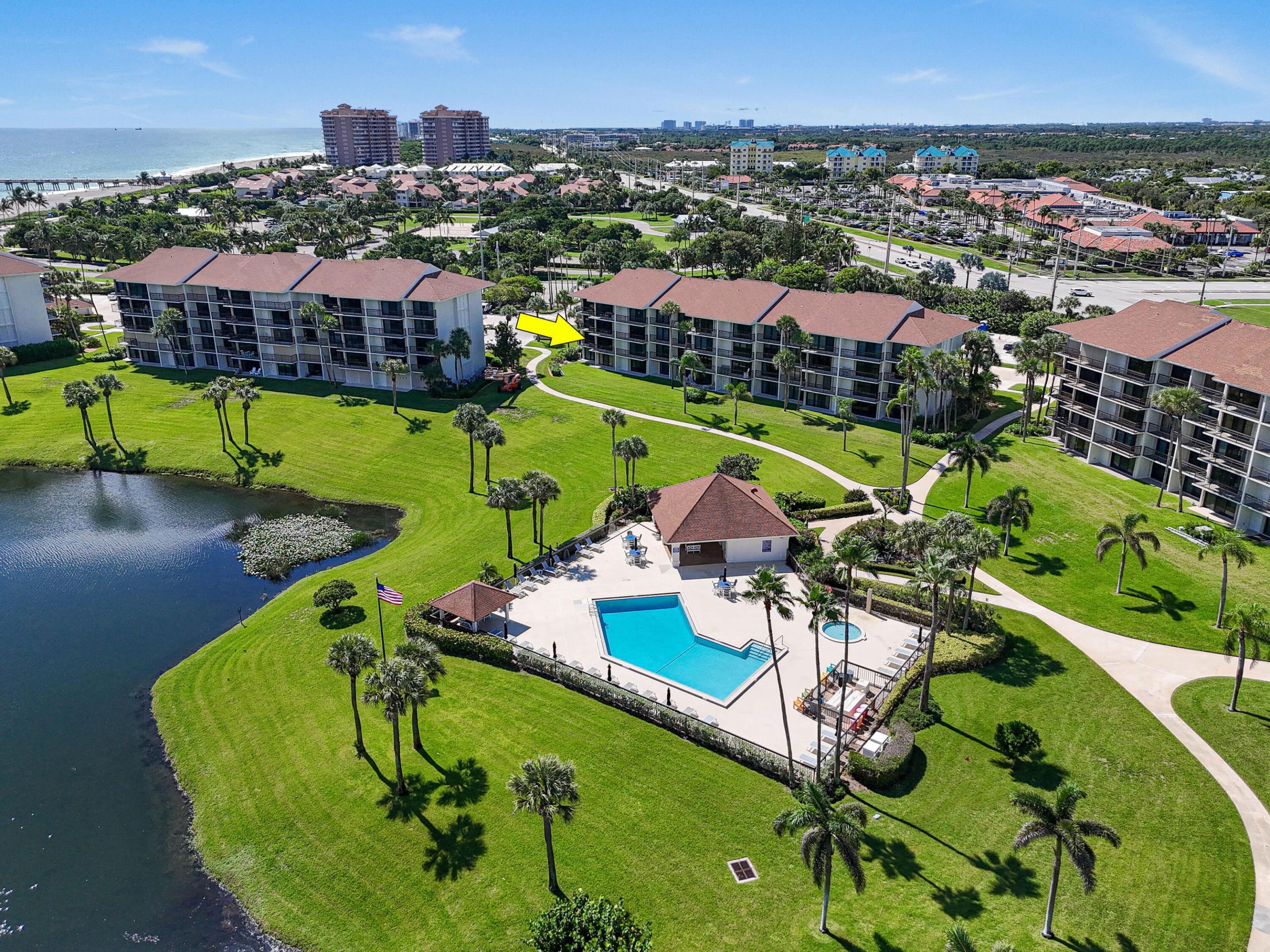 Aerial view of the condo building marked by an arrow, with a pool, lake, and ocean nearby.