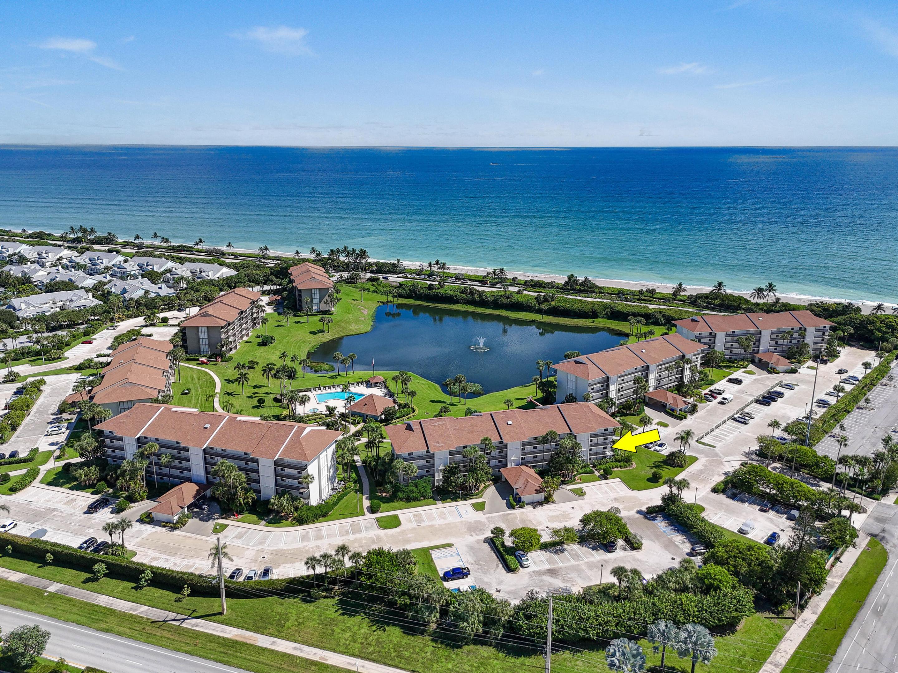 Aerial view of oceanfront condominiums with a lake and pool; a yellow arrow marks one building.