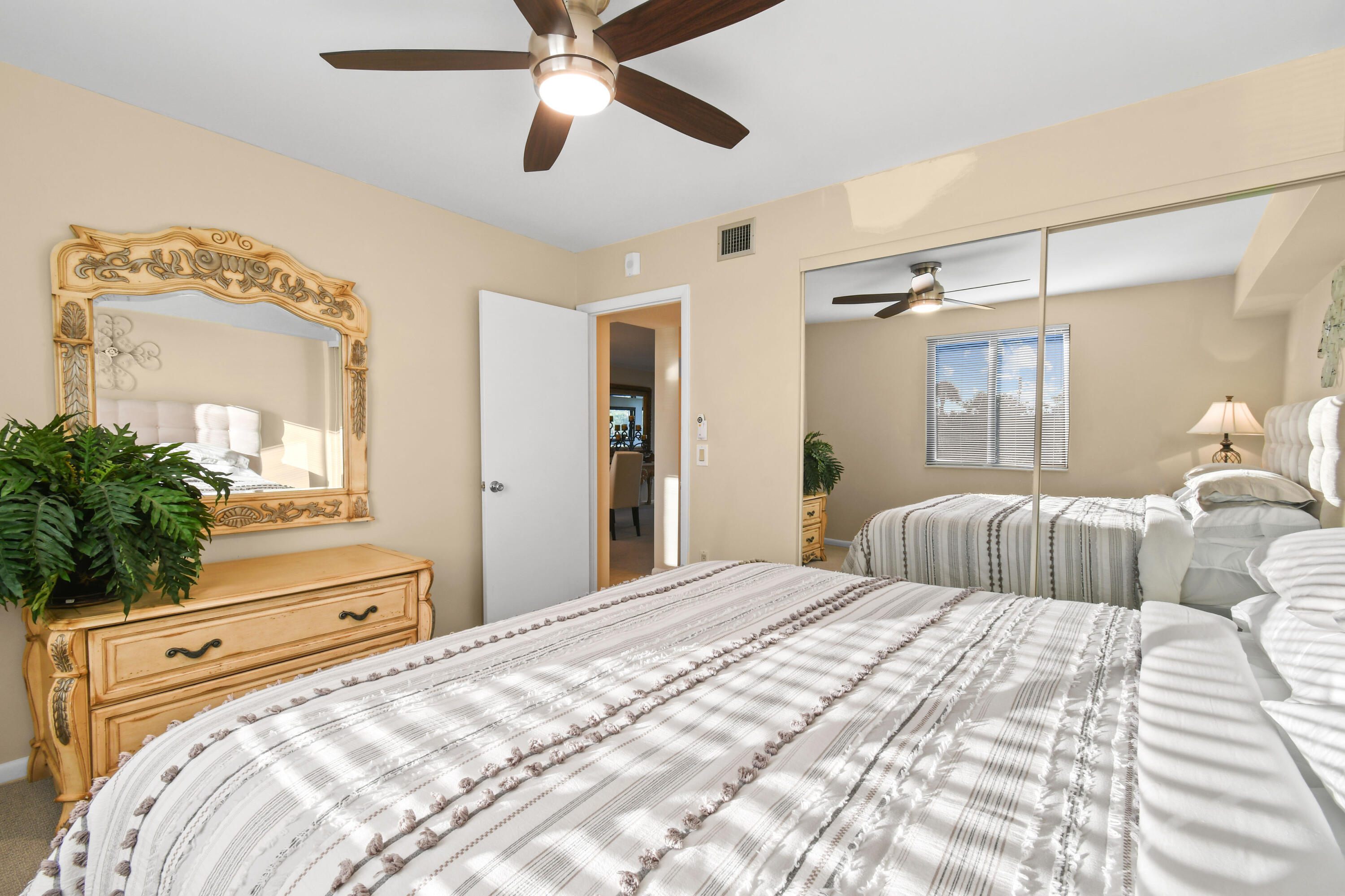 Bedroom with two striped beds, an ornate wood dresser and mirror, and mirrored closet doors.