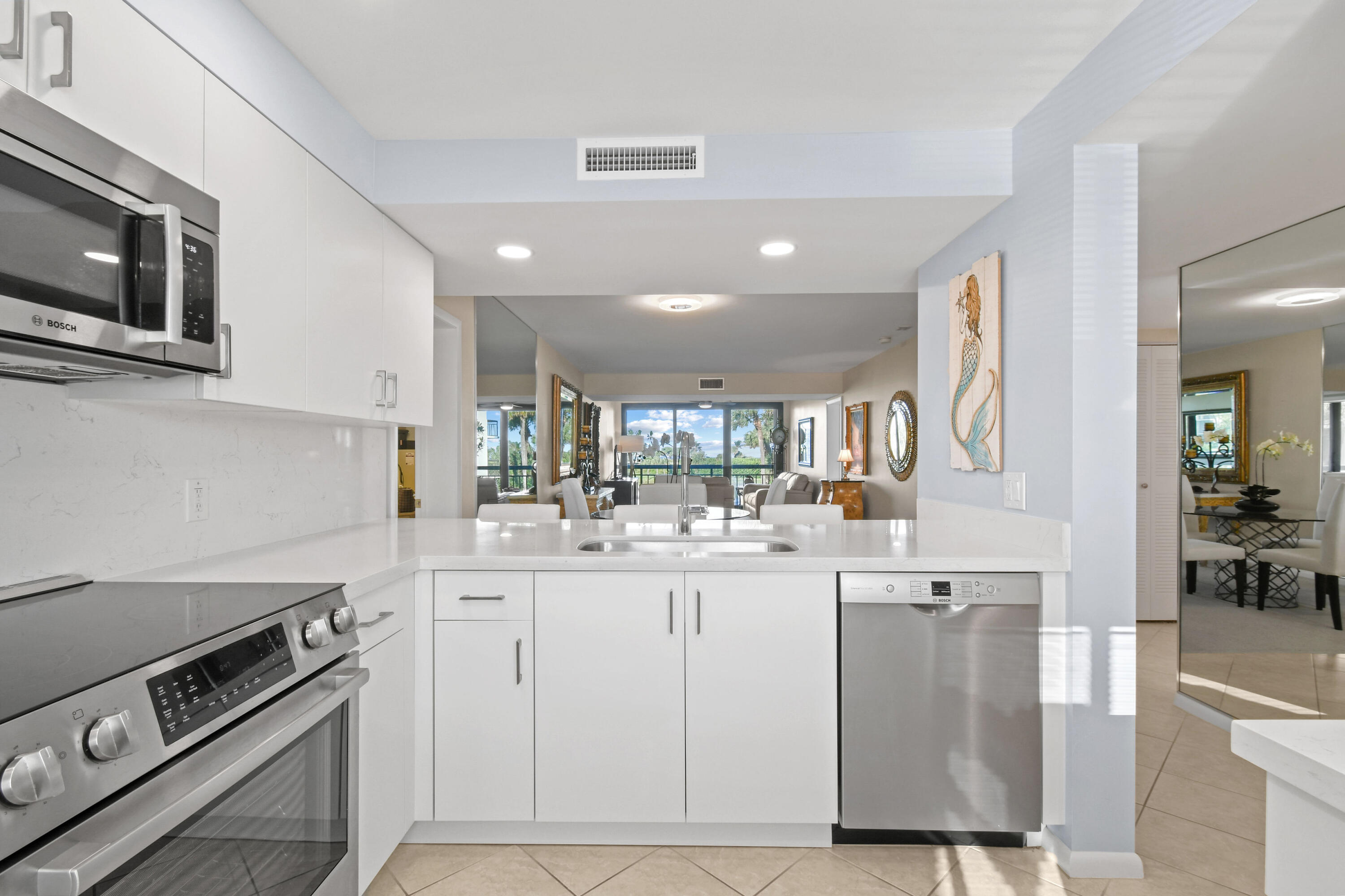 Modern white kitchen with stainless steel appliances and an open-plan living room overlooking the water.