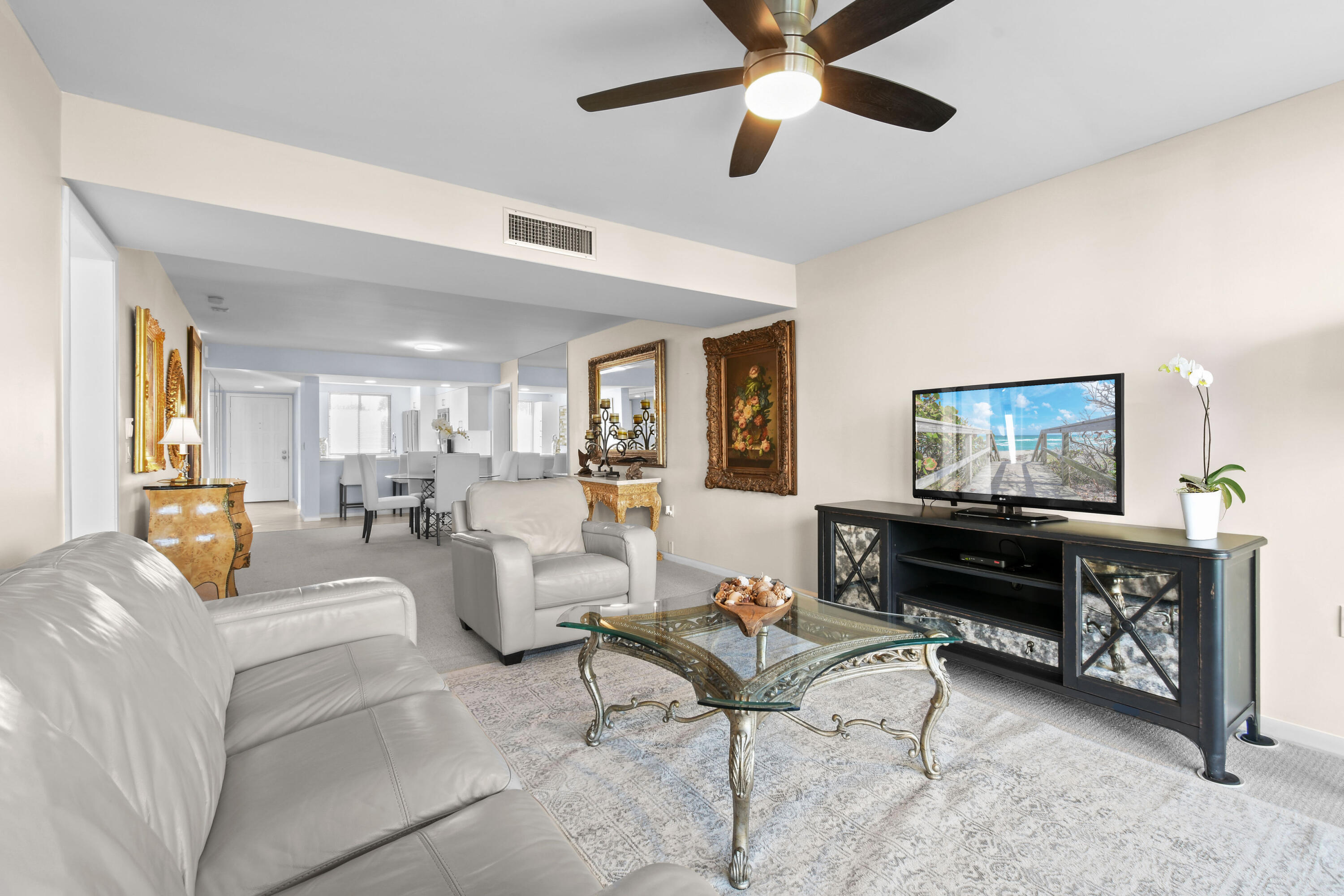 Furnished living room with white leather seating, ornate glass coffee table, and open dining area.