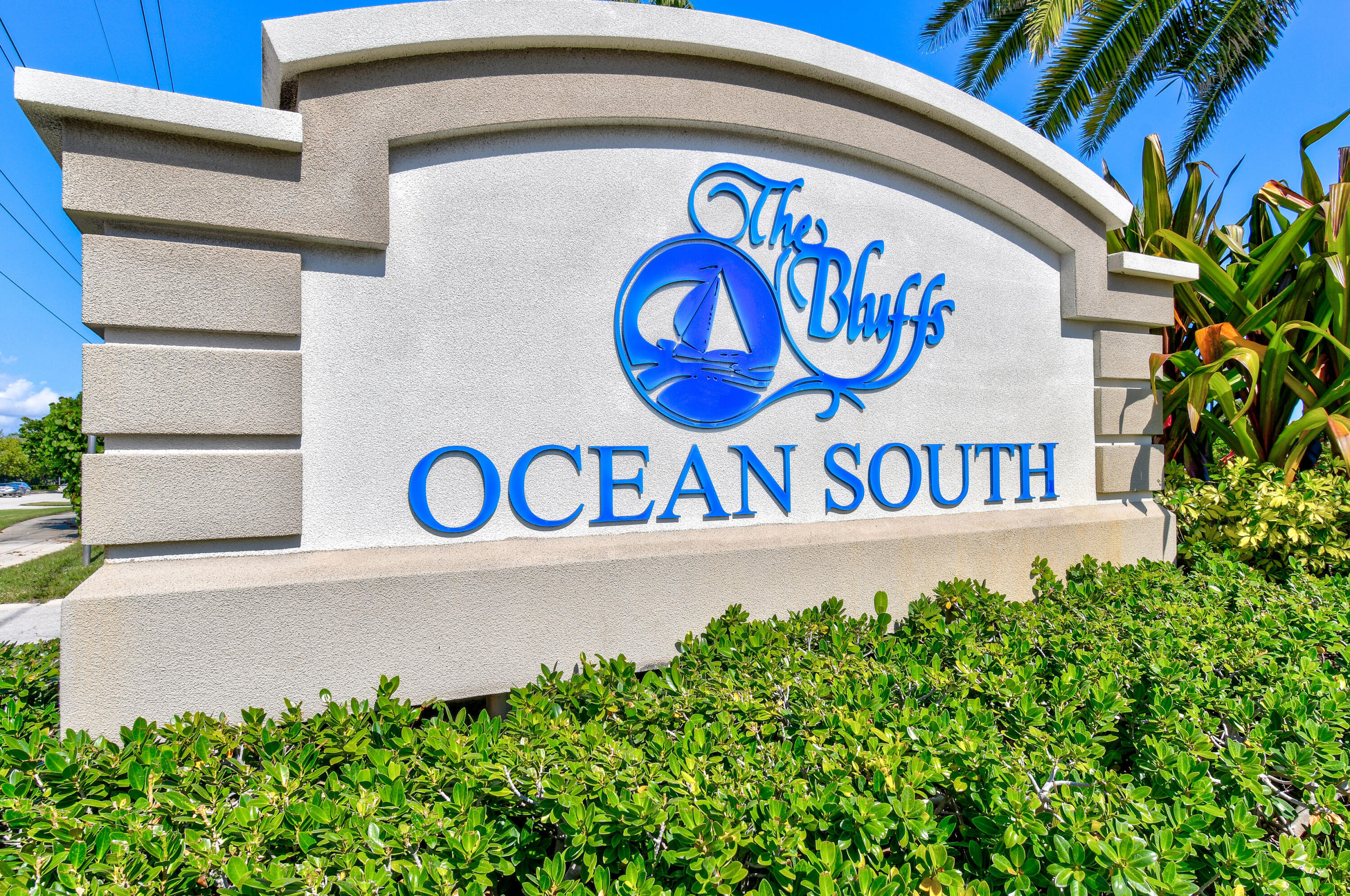 The Bluffs Ocean South entrance sign with a blue sailboat emblem, framed by tropical landscaping.