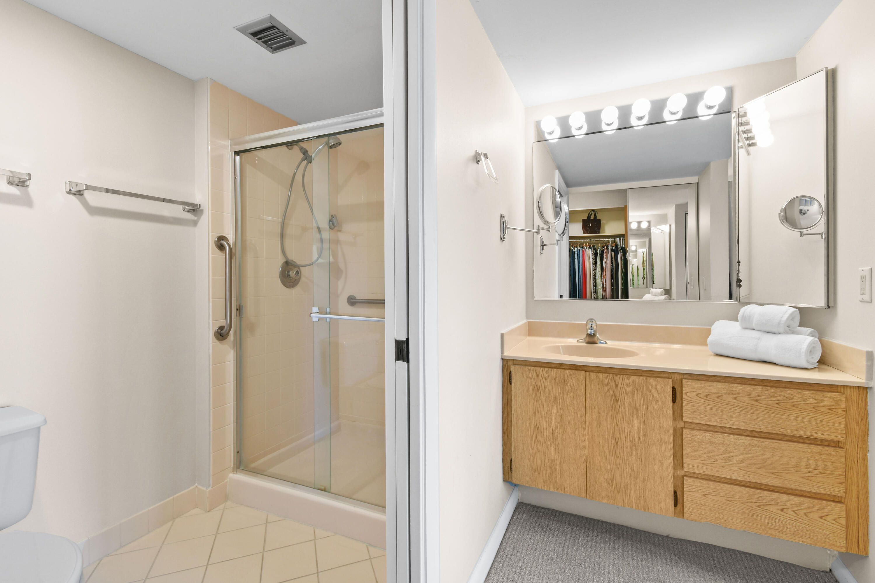 Bathroom with glass shower, oak vanity, and large illuminated mirror.