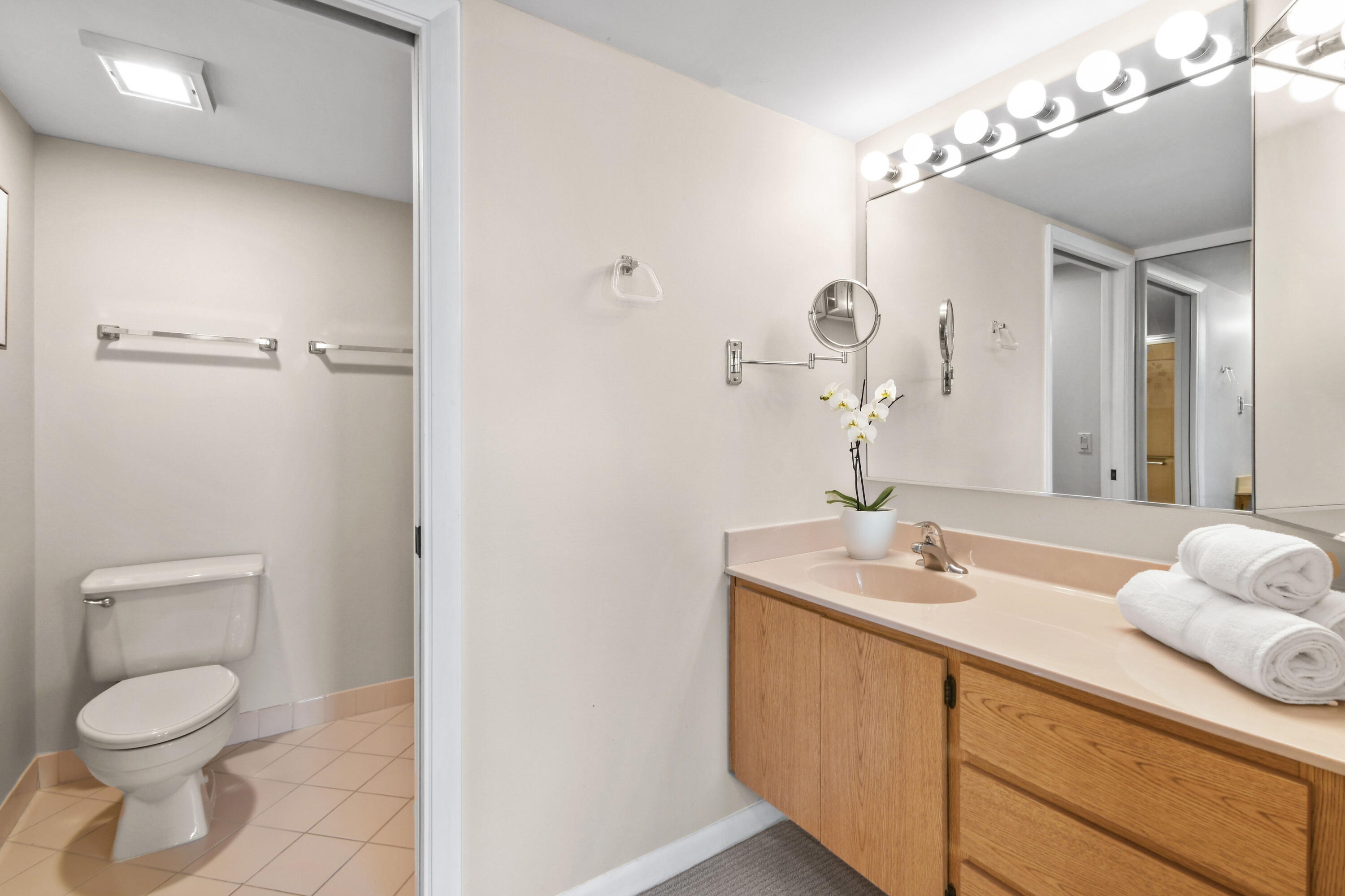 Bathroom with a wood vanity, illuminated mirror, toilet, and rolled white towels.
