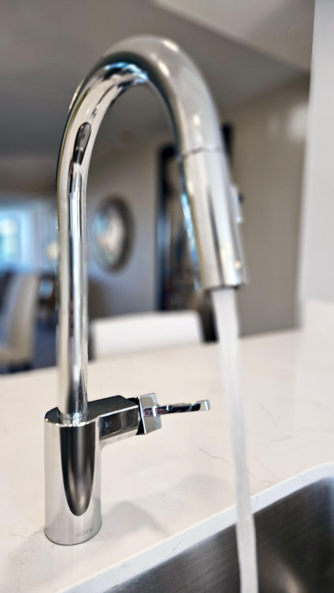 Chrome kitchen faucet running water over a white countertop.