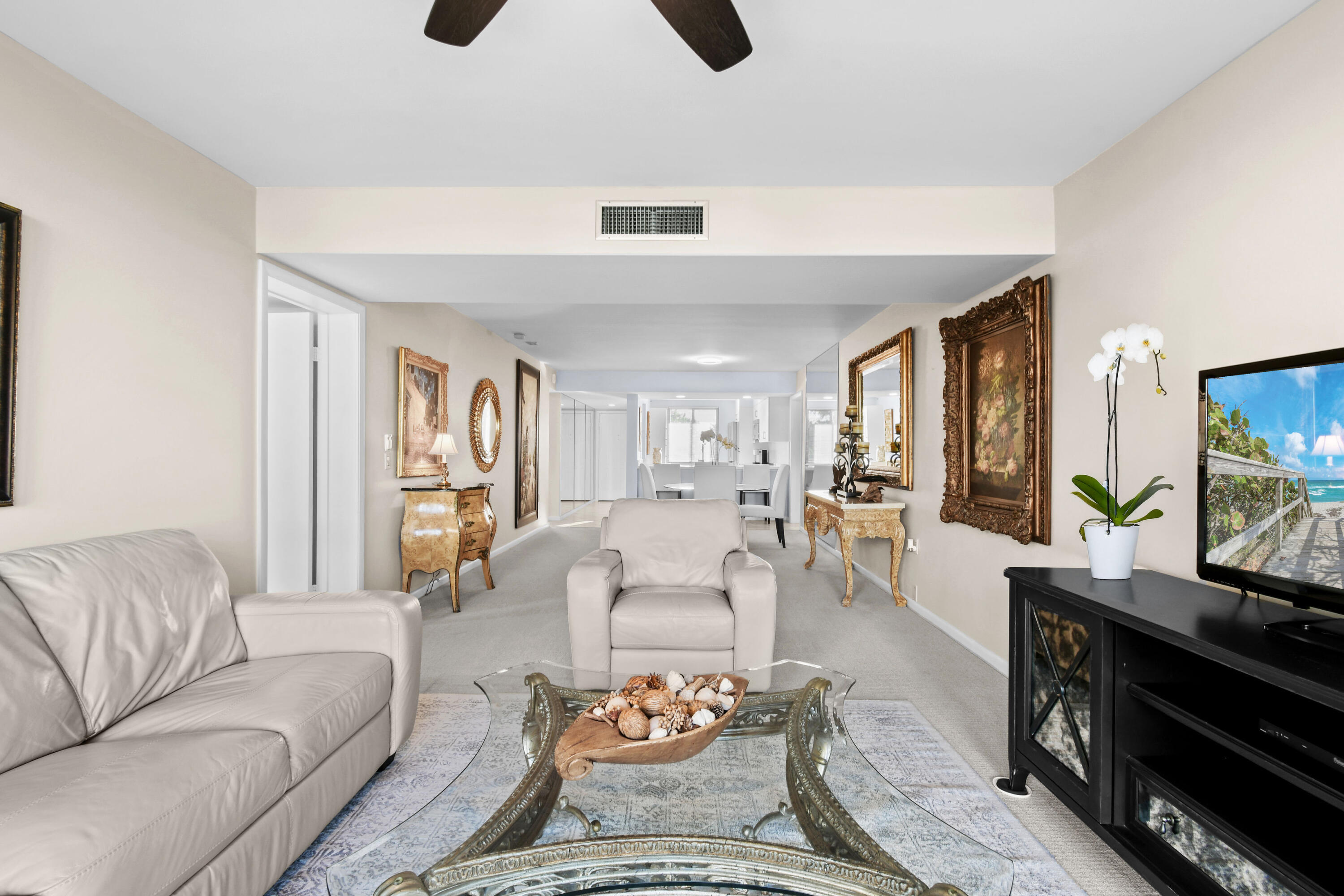Furnished living room with pale leather seating, ornate glass coffee table, and framed artwork.