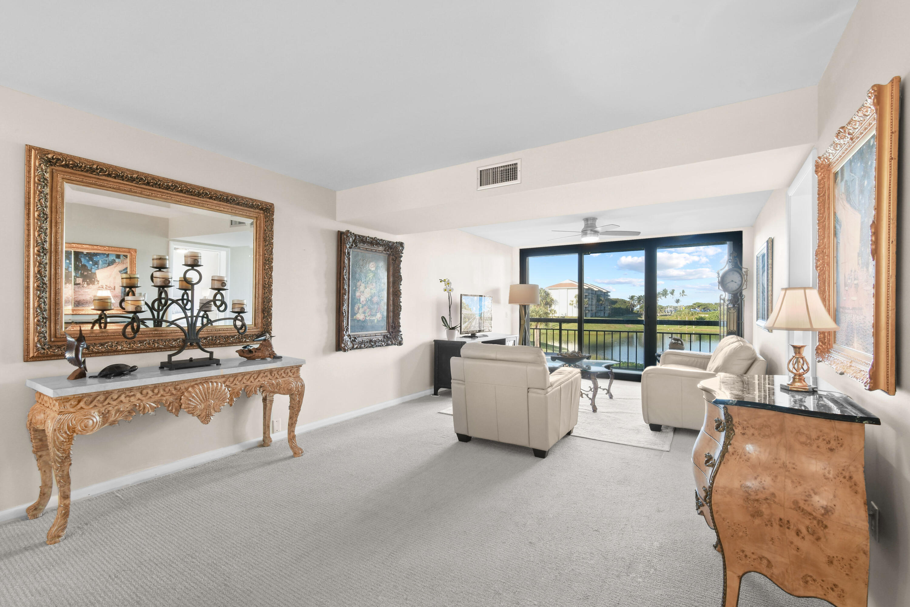 Living room with cream seating and ornate furnishings overlooking water through sliding glass doors.