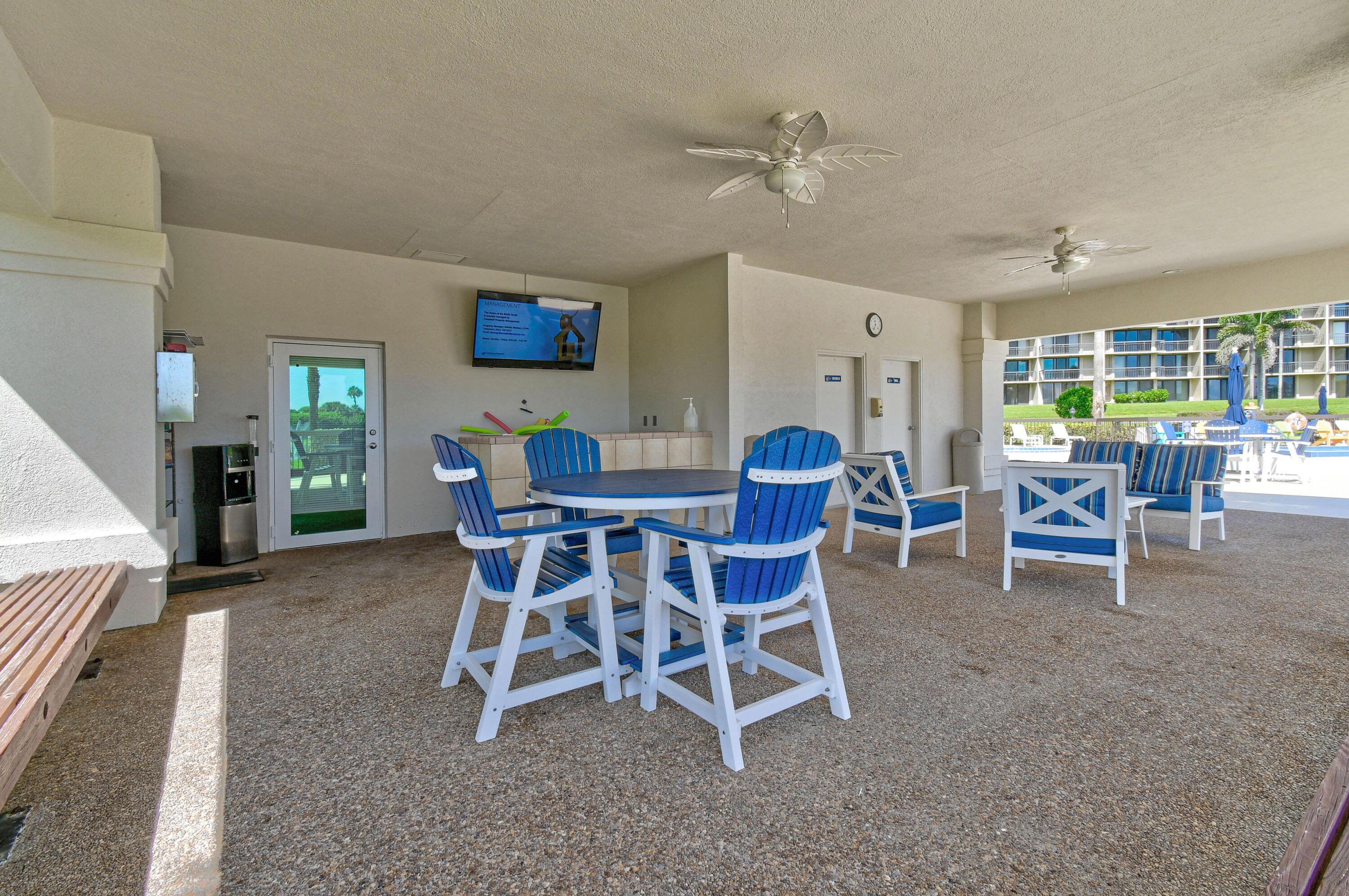 Covered patio with blue-and-white seating beside a pool and condominium building.