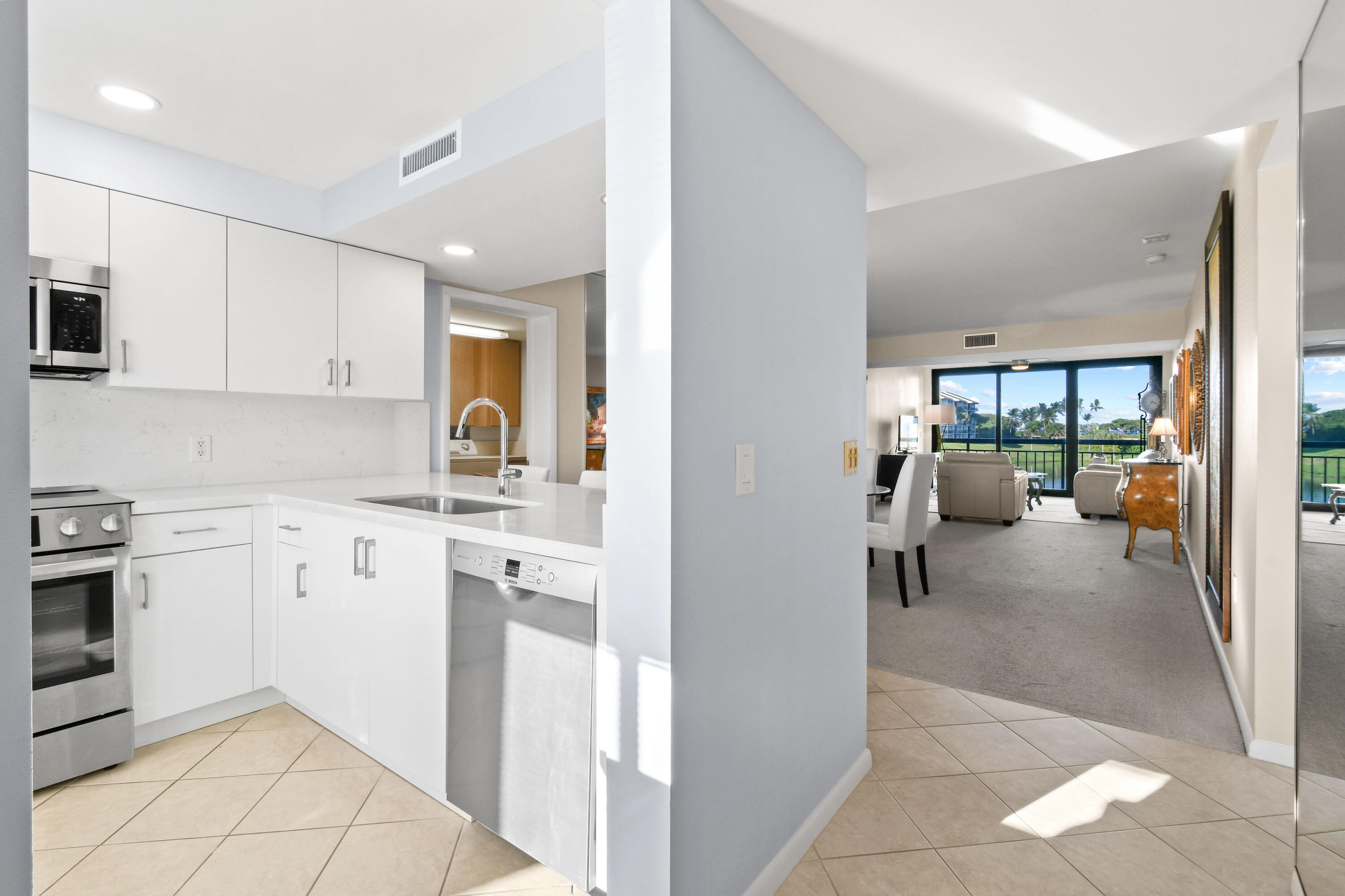 White modern kitchen opening to a furnished living area with sliding doors to a balcony.