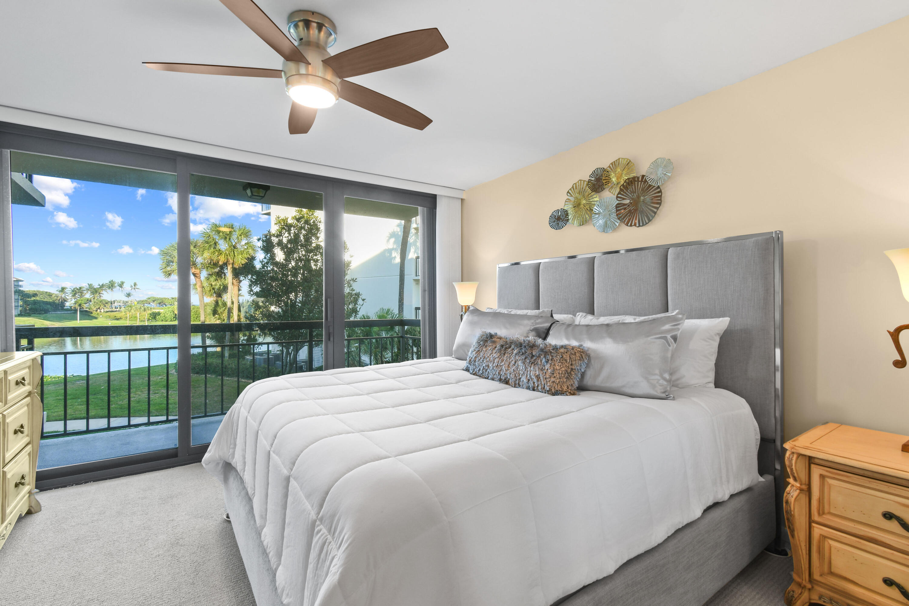 Bedroom with a gray upholstered bed and sliding doors overlooking water and palm trees.