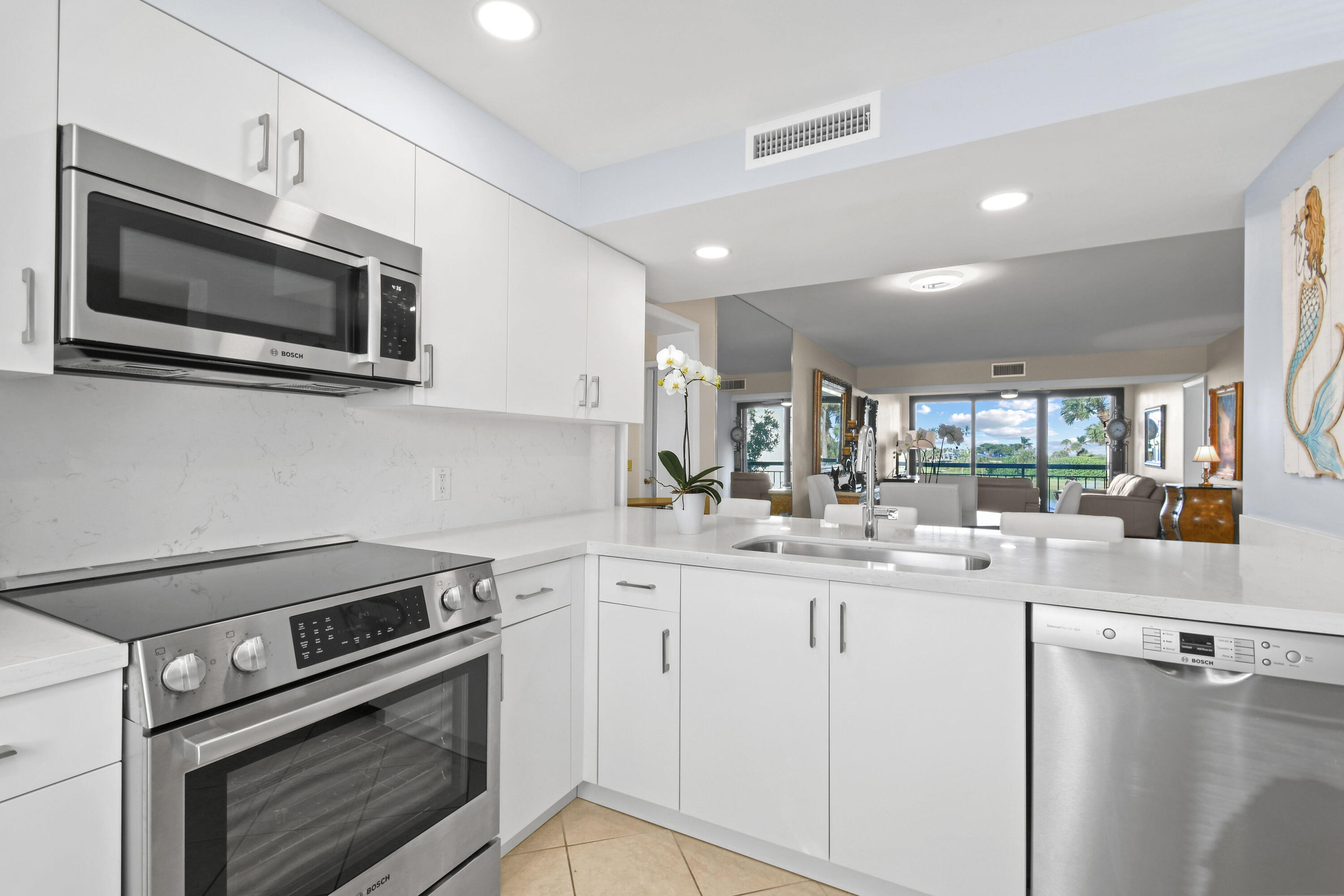 White kitchen with stainless steel appliances opens to a living room with a broad view through the windows.