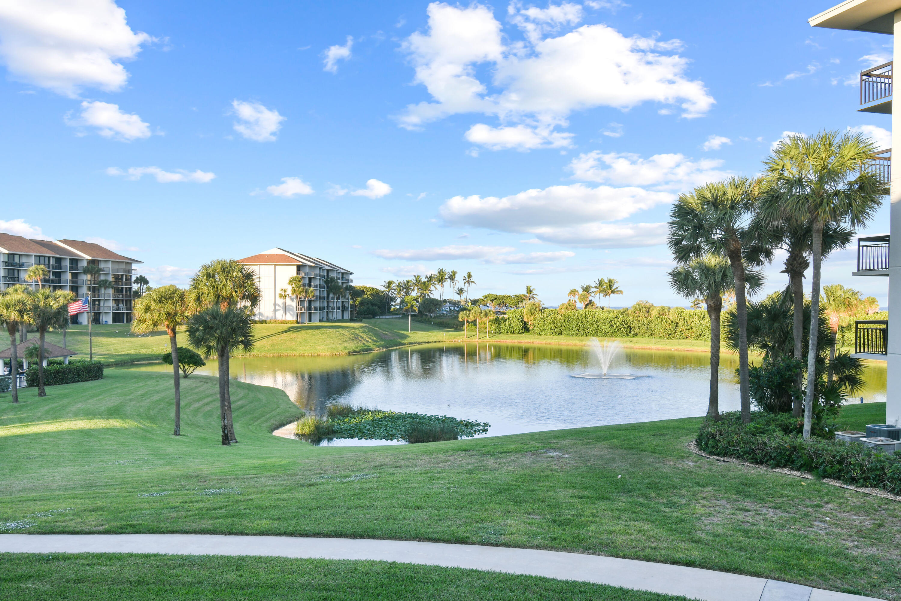 Landscaped condominium grounds with a fountain pond, palm trees, and neighboring buildings.