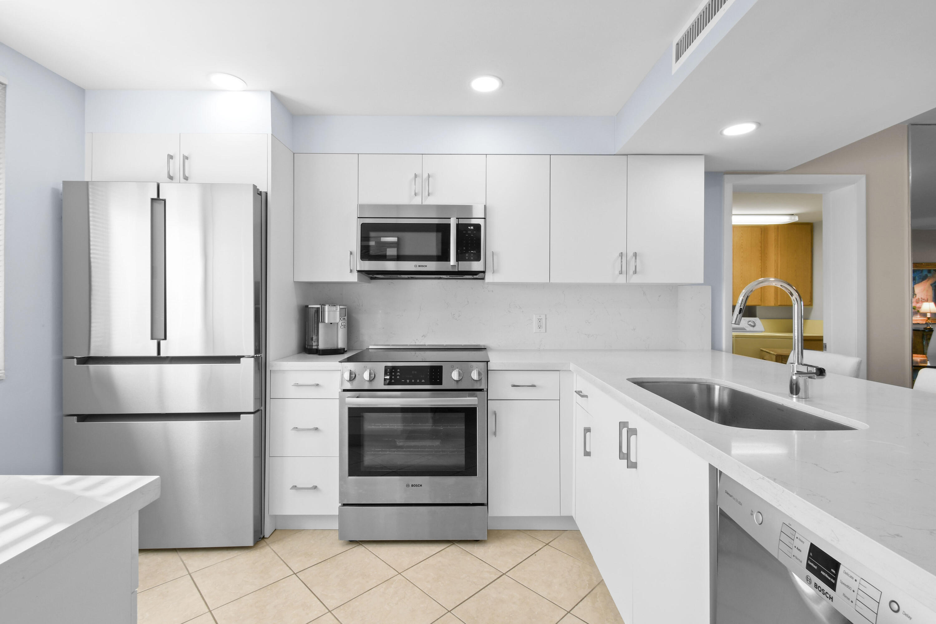 Modern white kitchen with stainless steel appliances and a long island with sink.