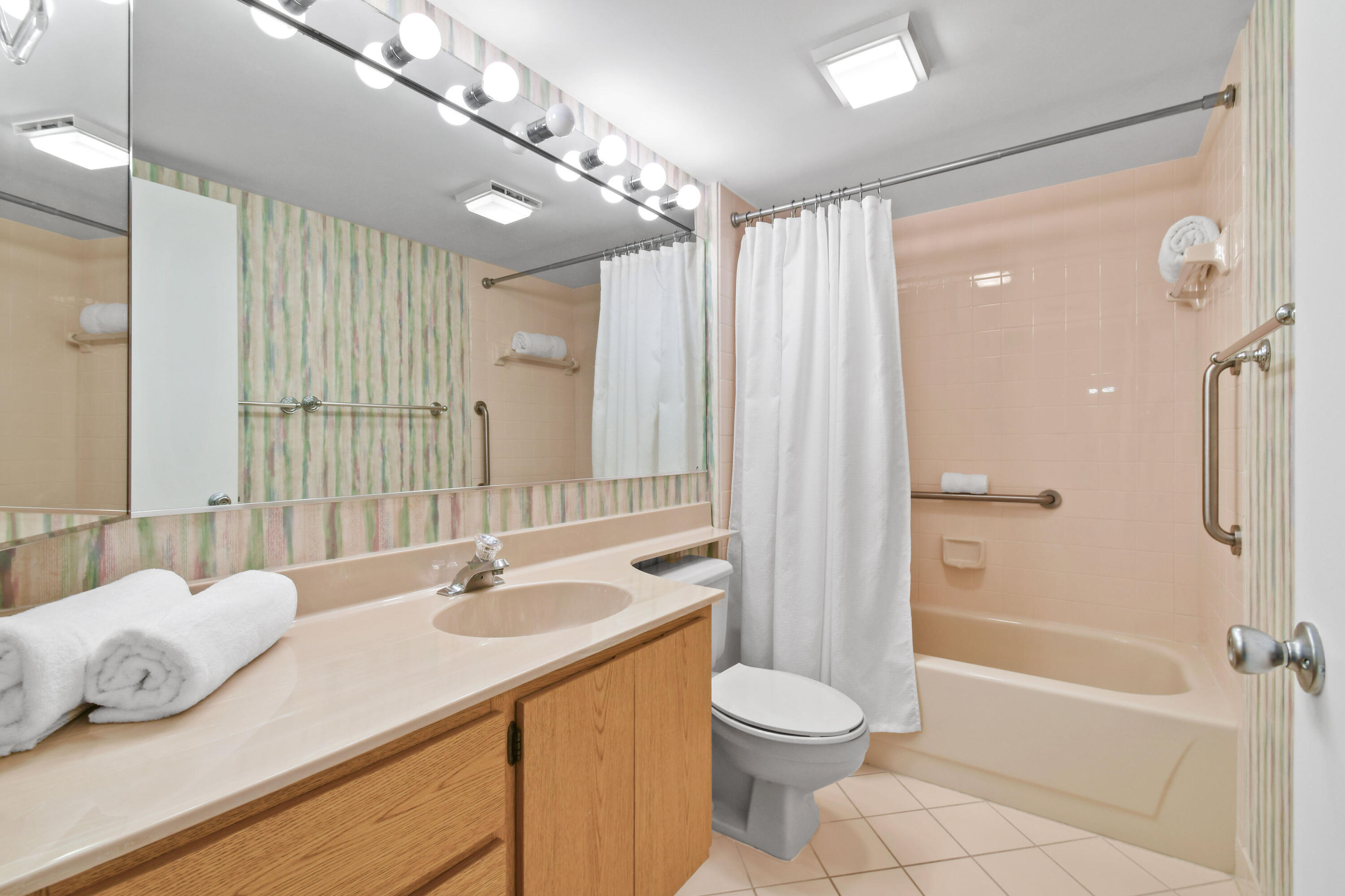 Bathroom with a long wood vanity, large mirror, and peach-tiled bathtub behind a white shower curtain.
