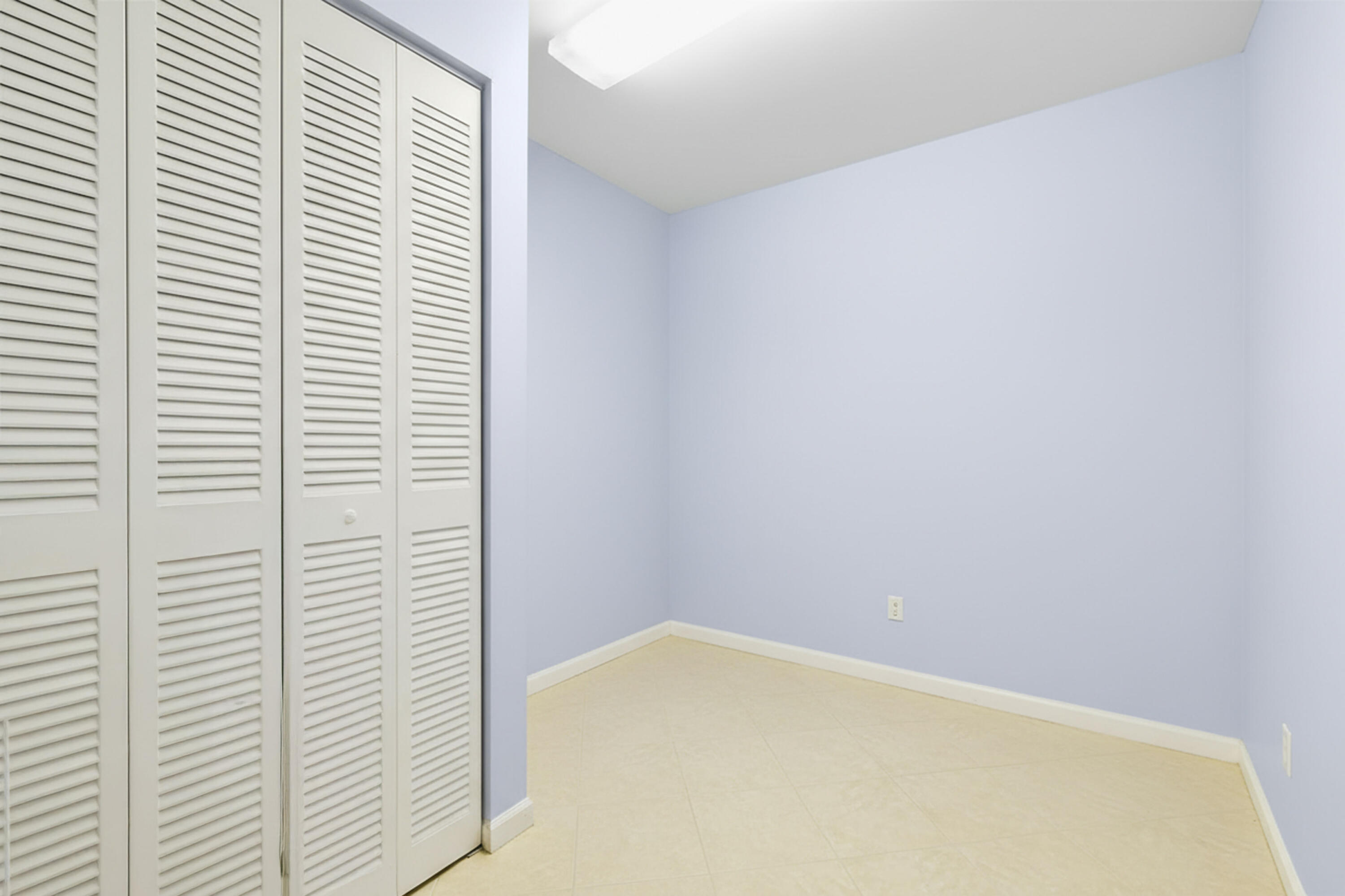 Empty room with pale lavender walls, beige tile floor, and white louvered closet doors.