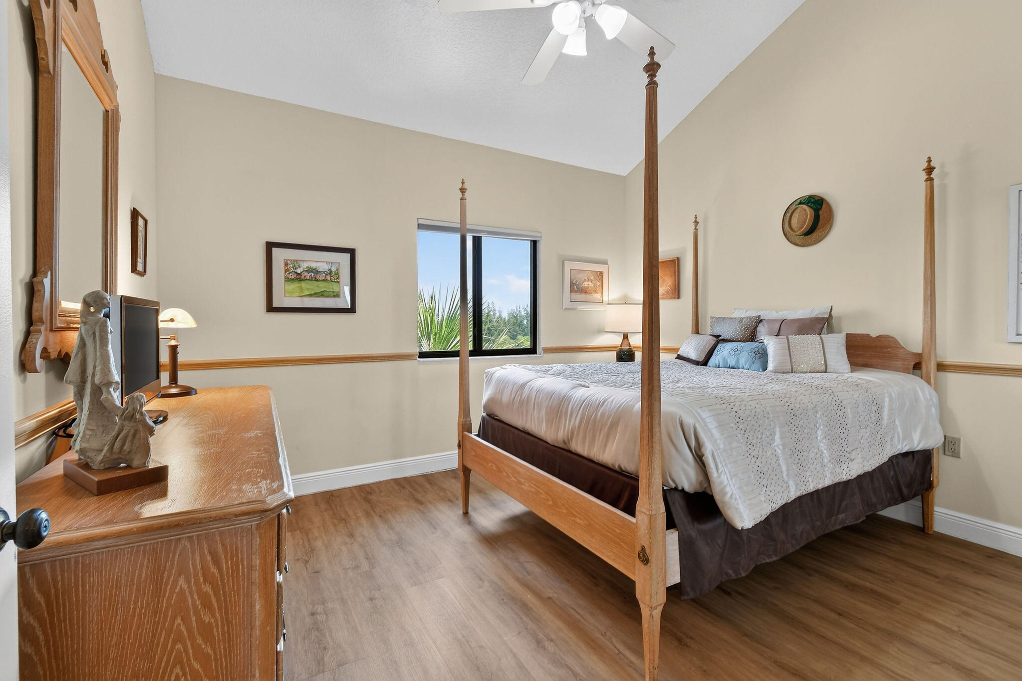 Bedroom with a wooden four-poster bed, dresser, and window overlooking greenery.