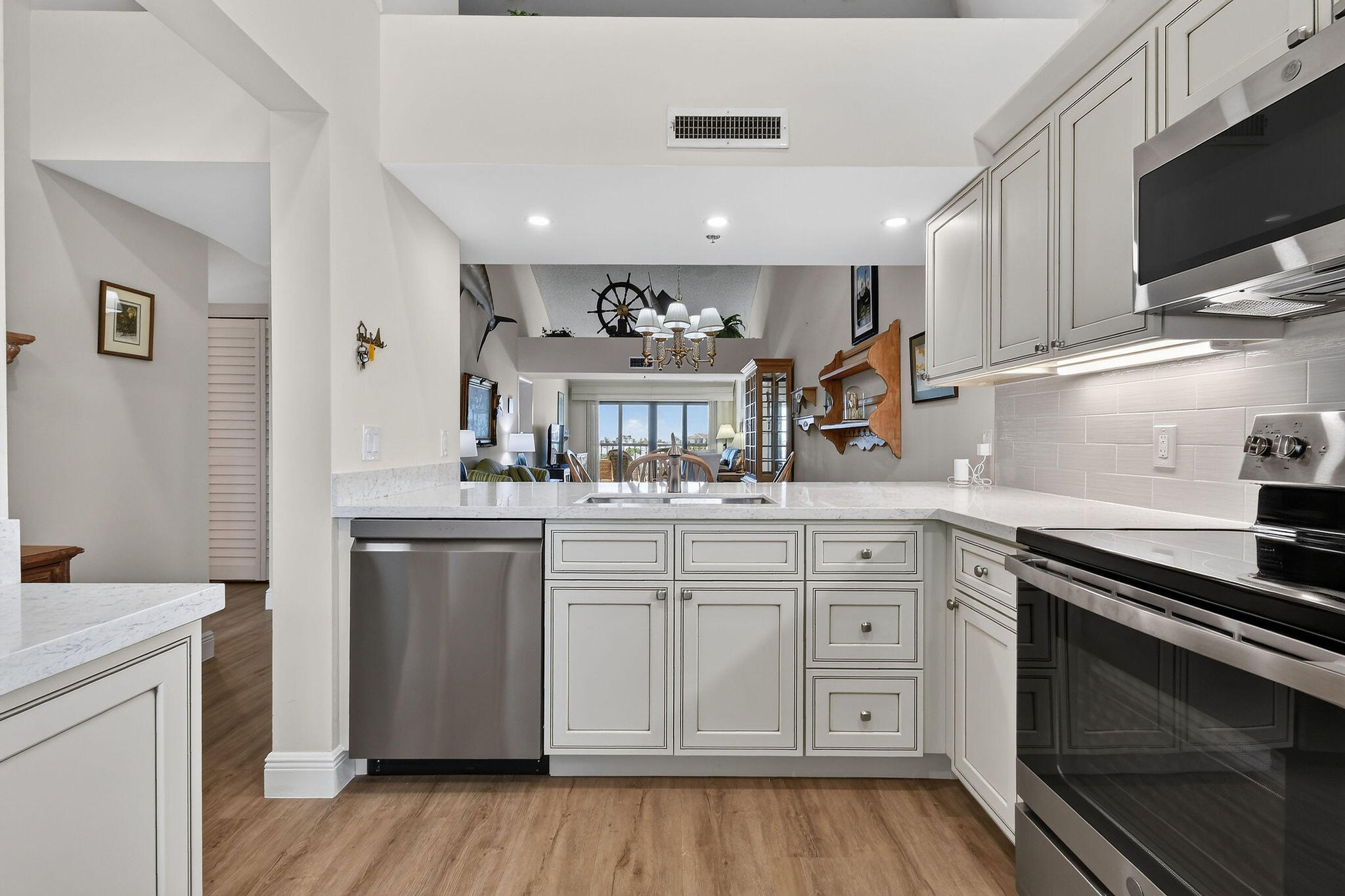 Bright white kitchen with stone counters and stainless appliances opening to a furnished living area.