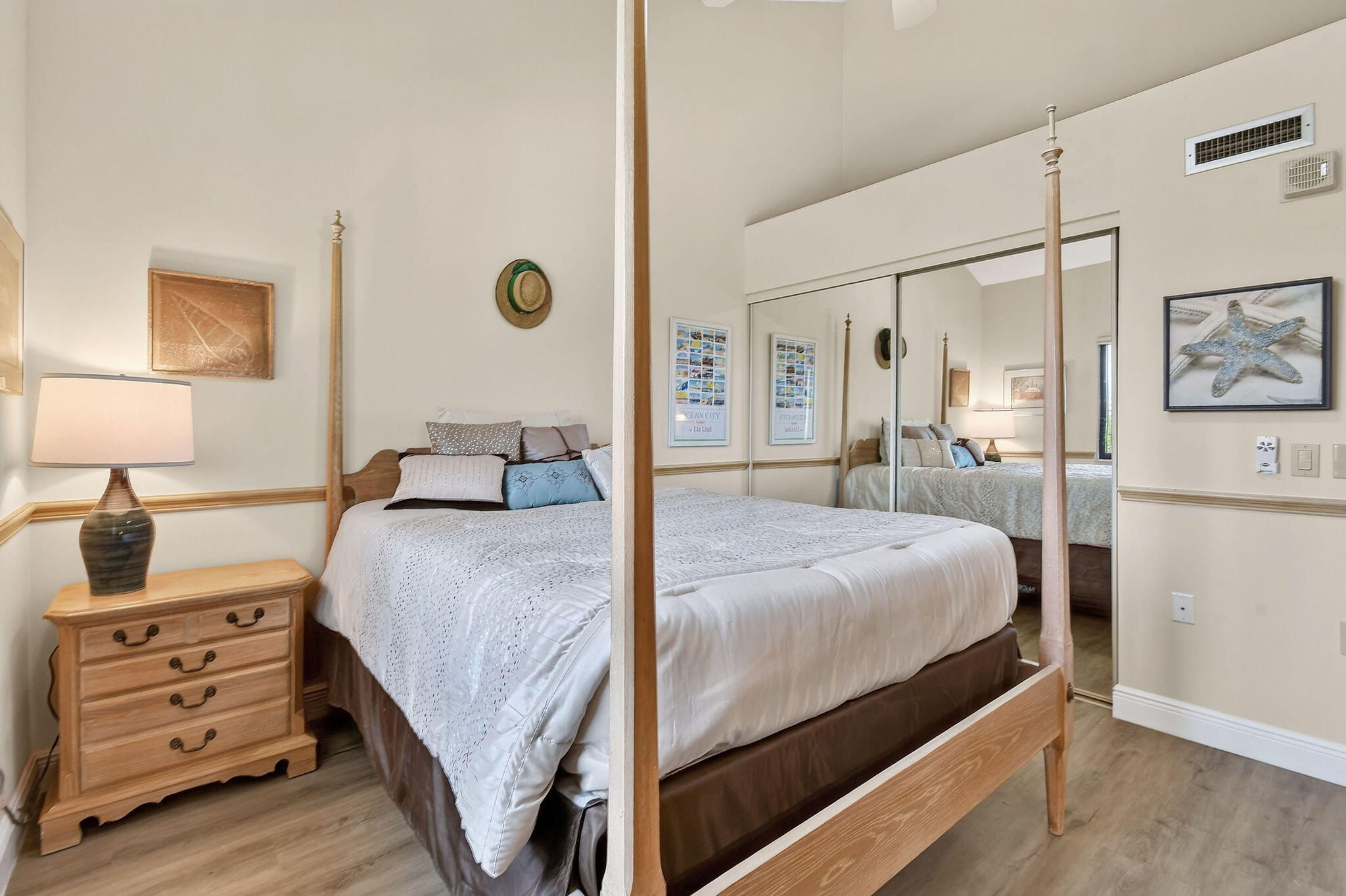 Furnished bedroom with a four-poster bed, mirrored closet doors, and coastal decor.