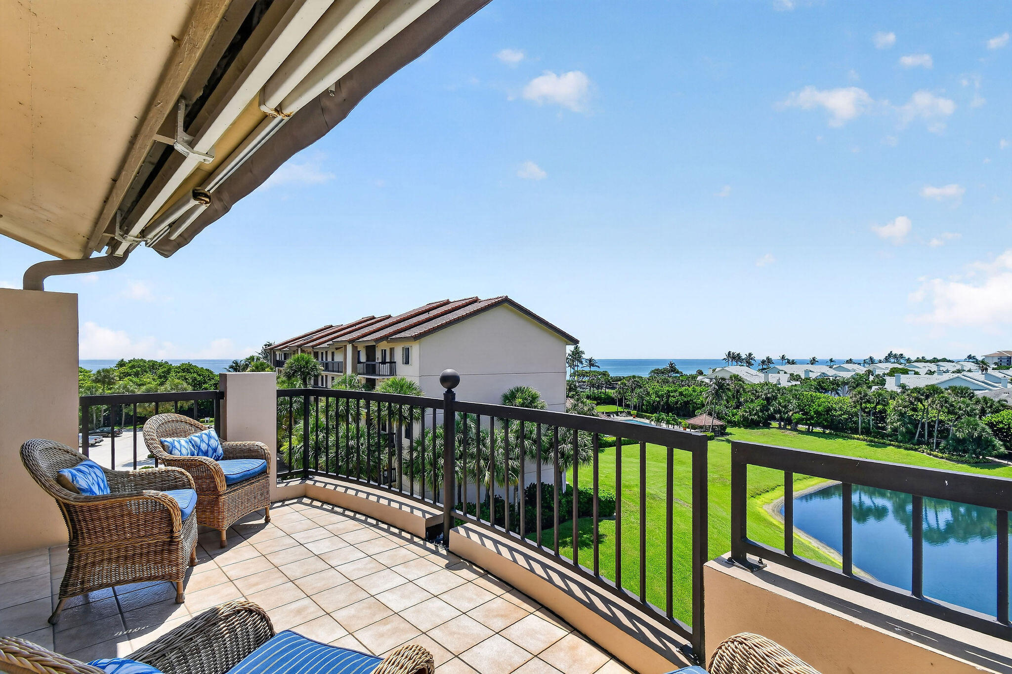 Furnished balcony overlooking a pond, palm trees, and ocean.