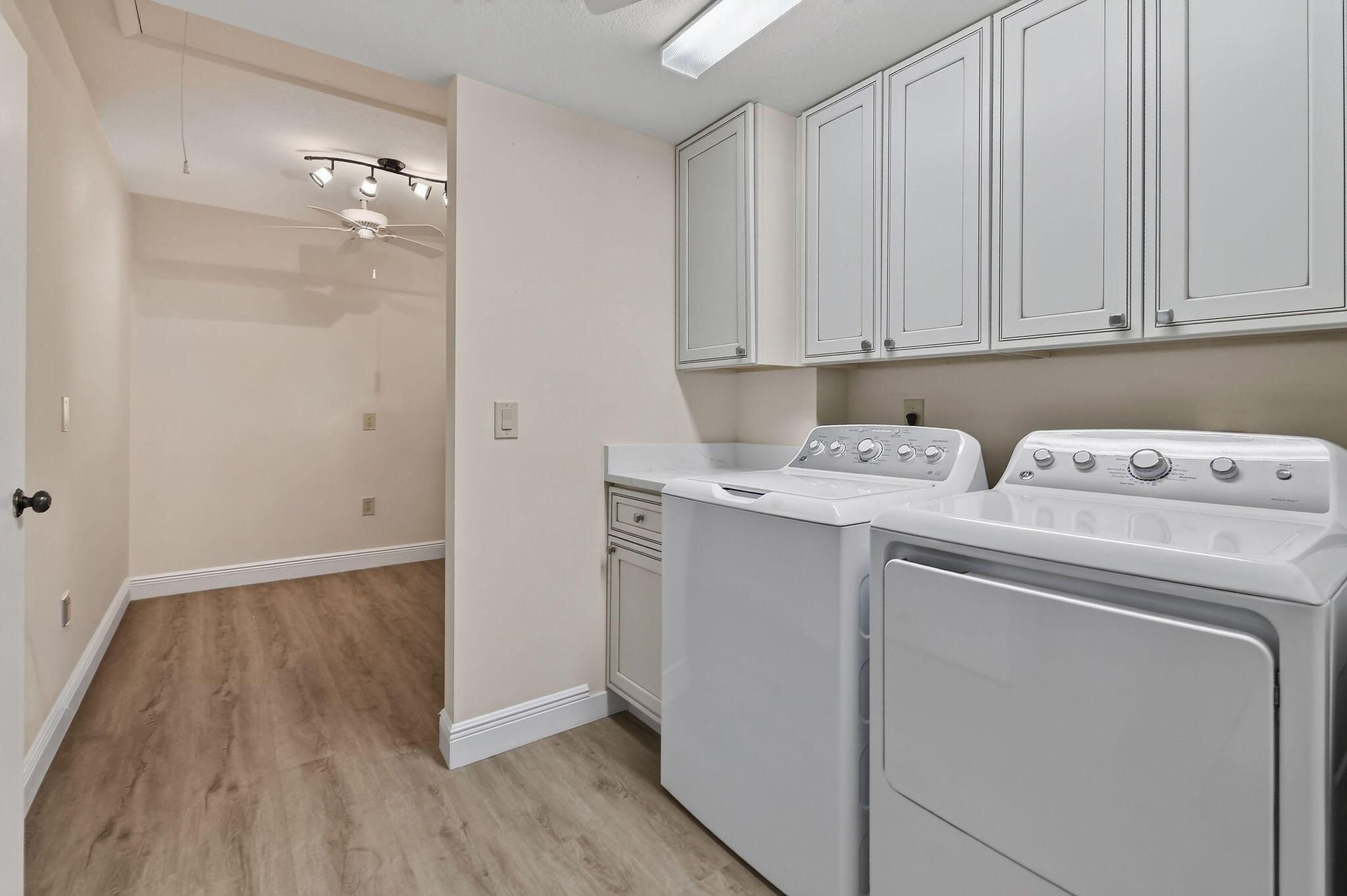 Laundry room with white washer and dryer, overhead cabinets, and wood-look flooring.