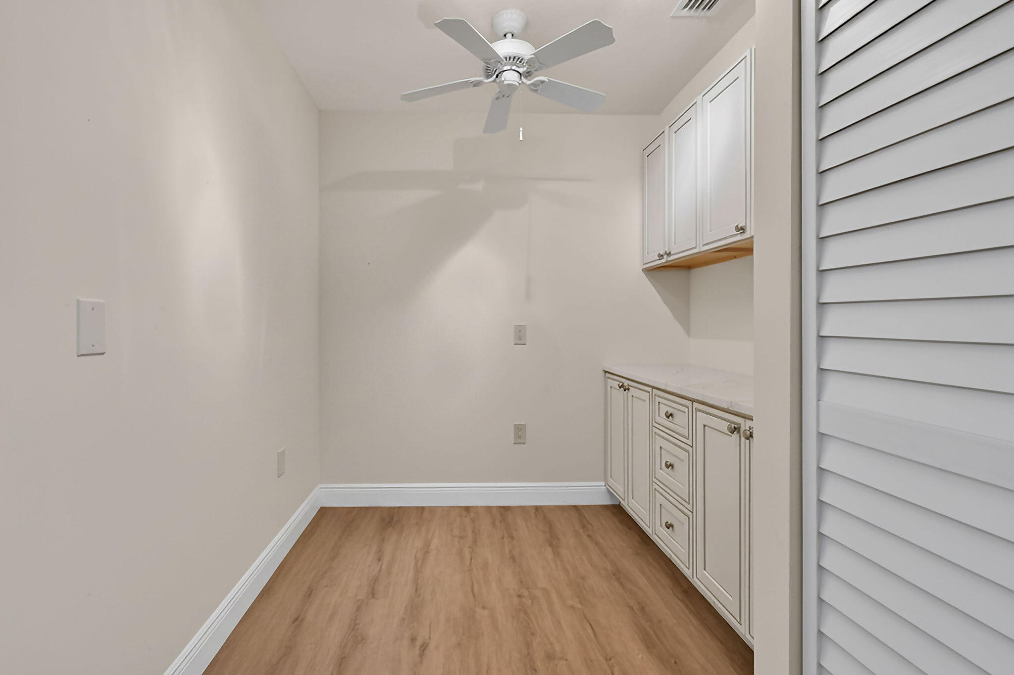 Empty room with wood-look flooring, built-in white cabinets, and a ceiling fan.