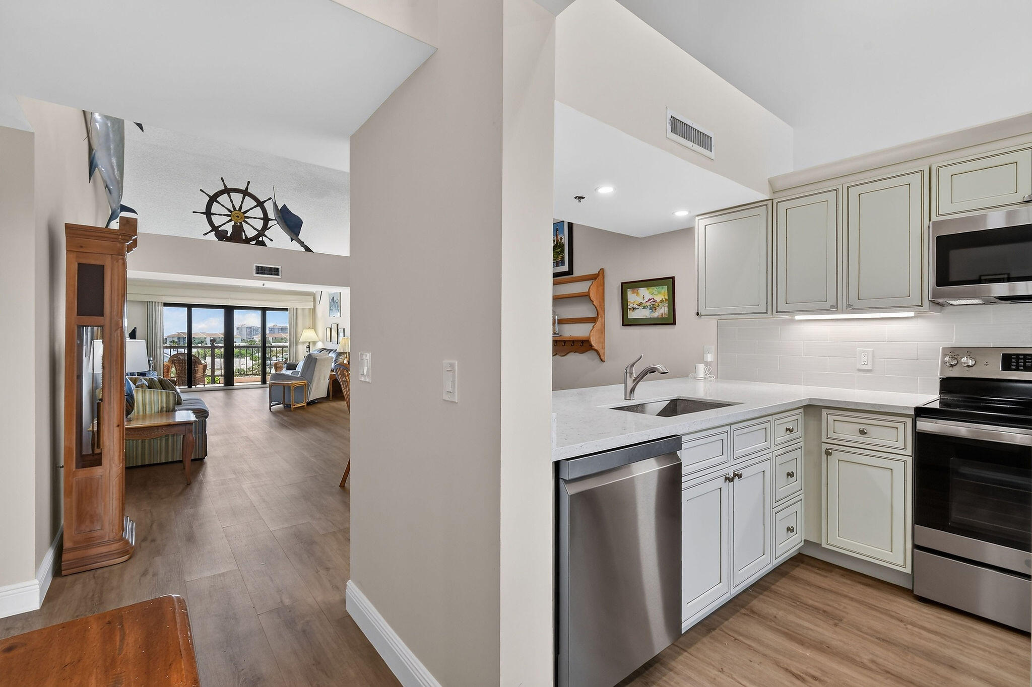 Condominium kitchen with white cabinets and stainless appliances, opening to a furnished living room and balcony.