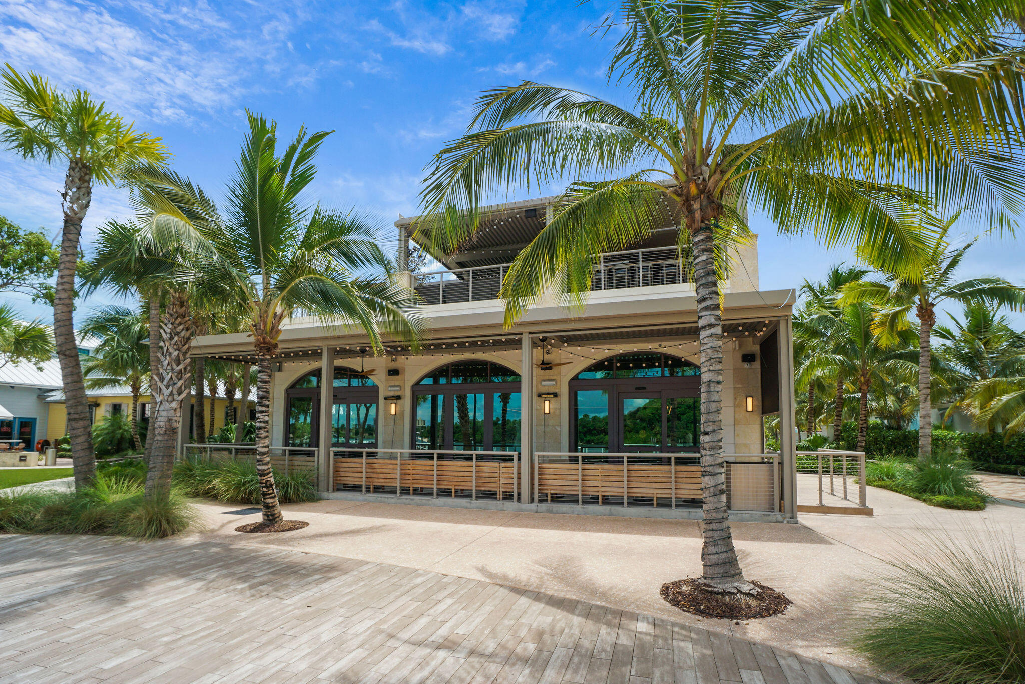 Modern coastal building with a covered patio and balcony, framed by palm trees.