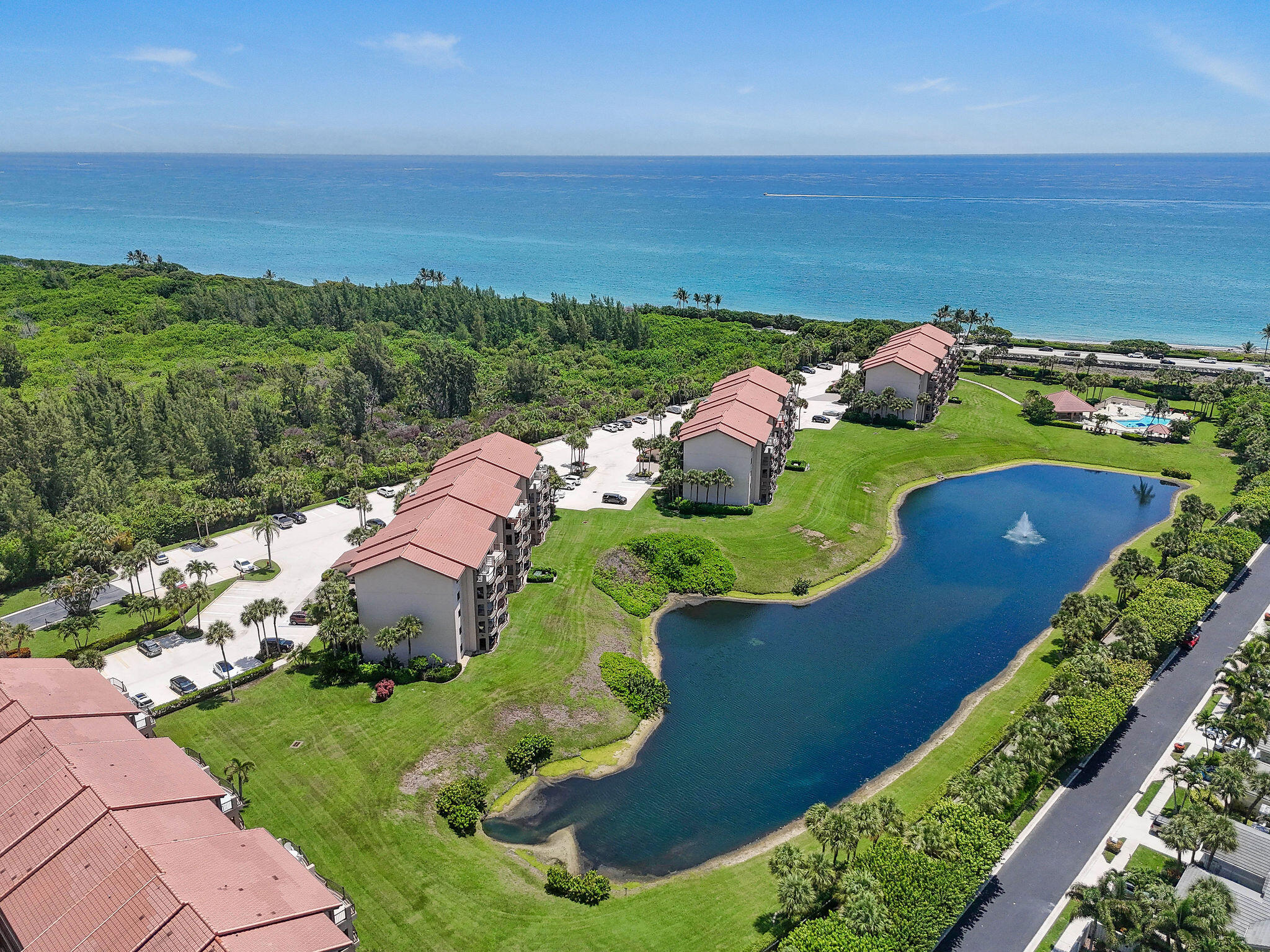 Aerial view of coastal condominiums, with a fountain pond and oceanfront beyond.