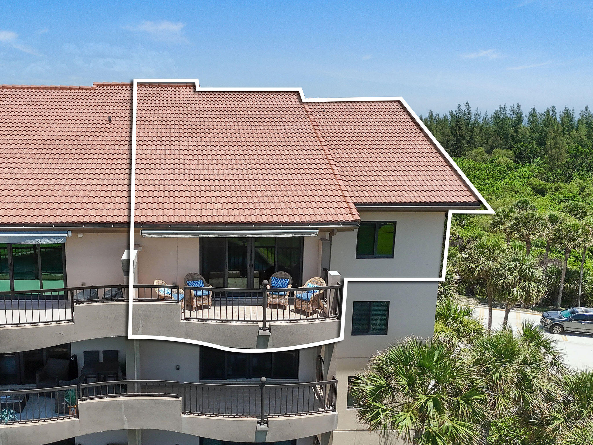 Condominium unit outlined on a red-tile-roof building, with a furnished balcony and surrounding palms.