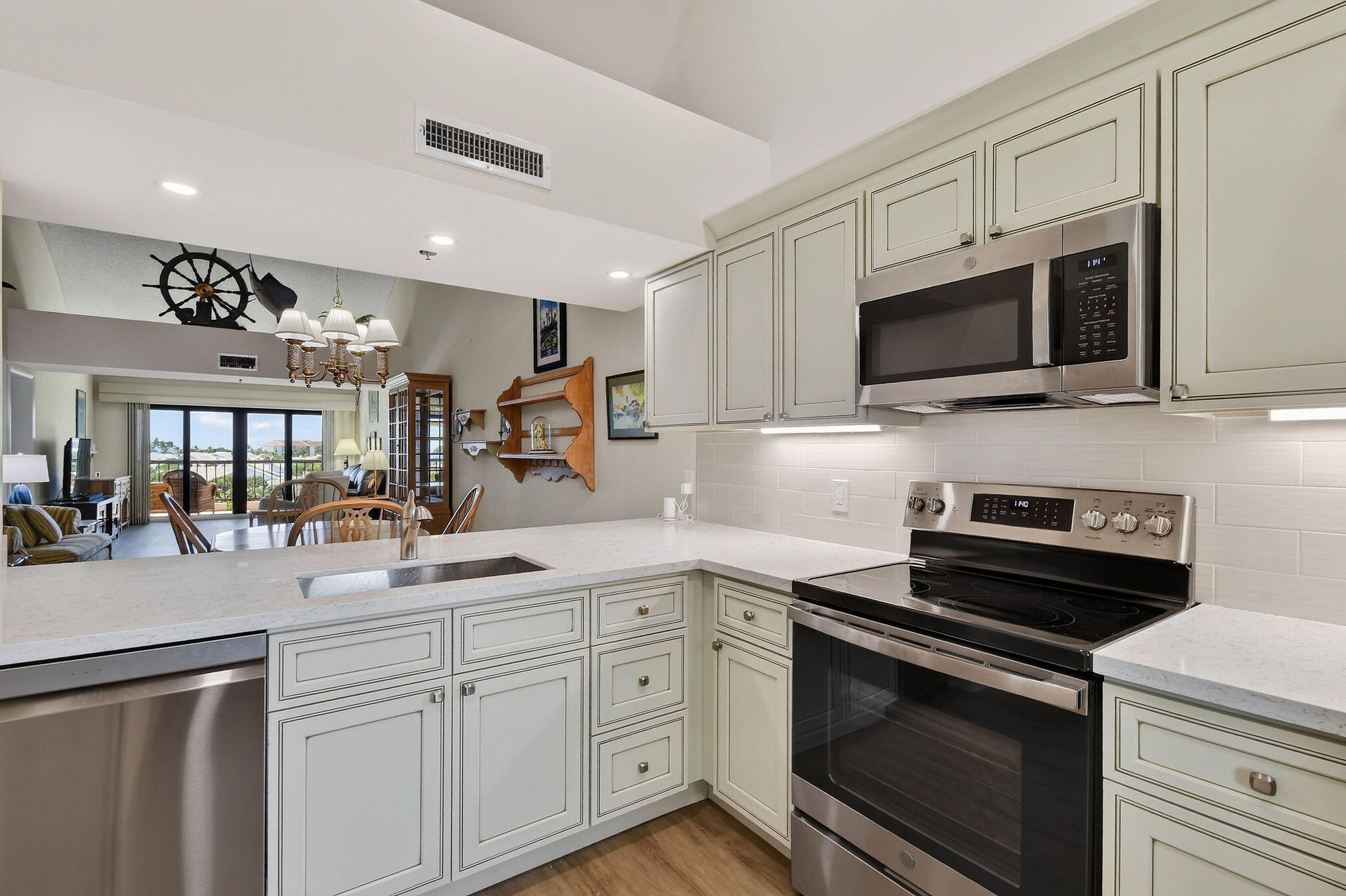 Kitchen with cream paneled cabinets, white counters, stainless steel appliances, and an open dining area.