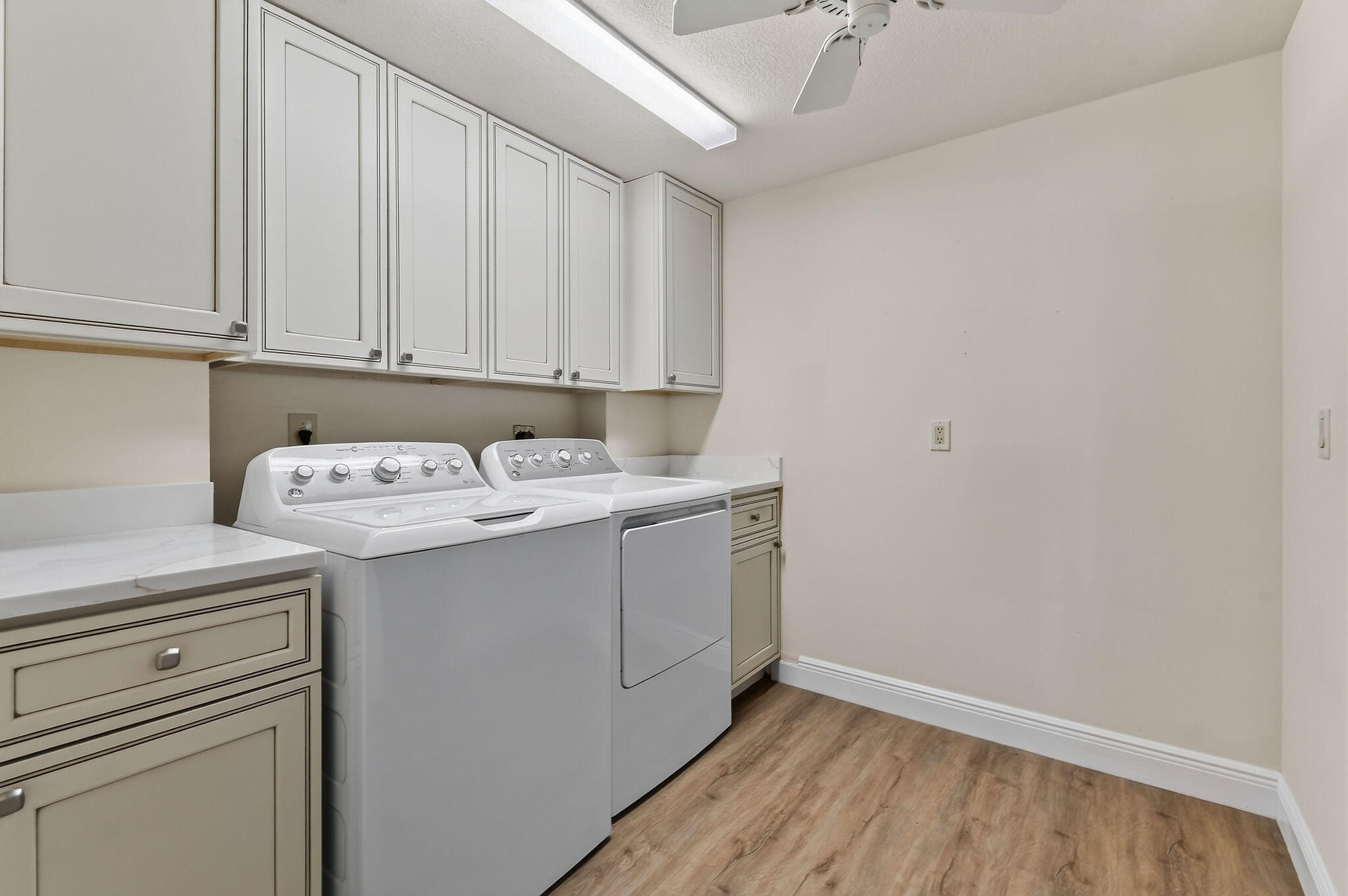 Laundry room with a top-loading washer, dryer, upper cabinets, and wood-look flooring.