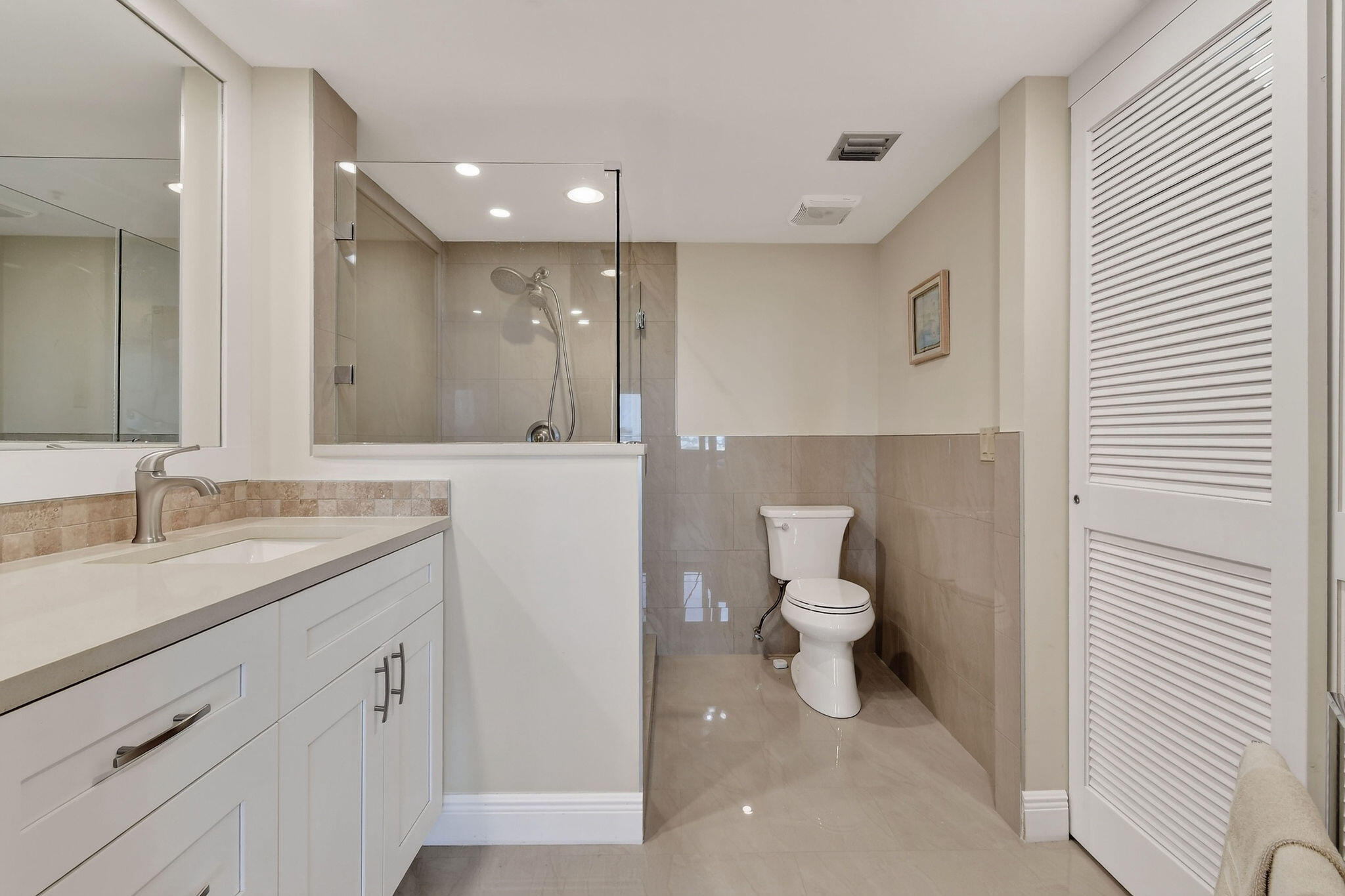 Bathroom with a white vanity, glass-enclosed shower, and beige tile.