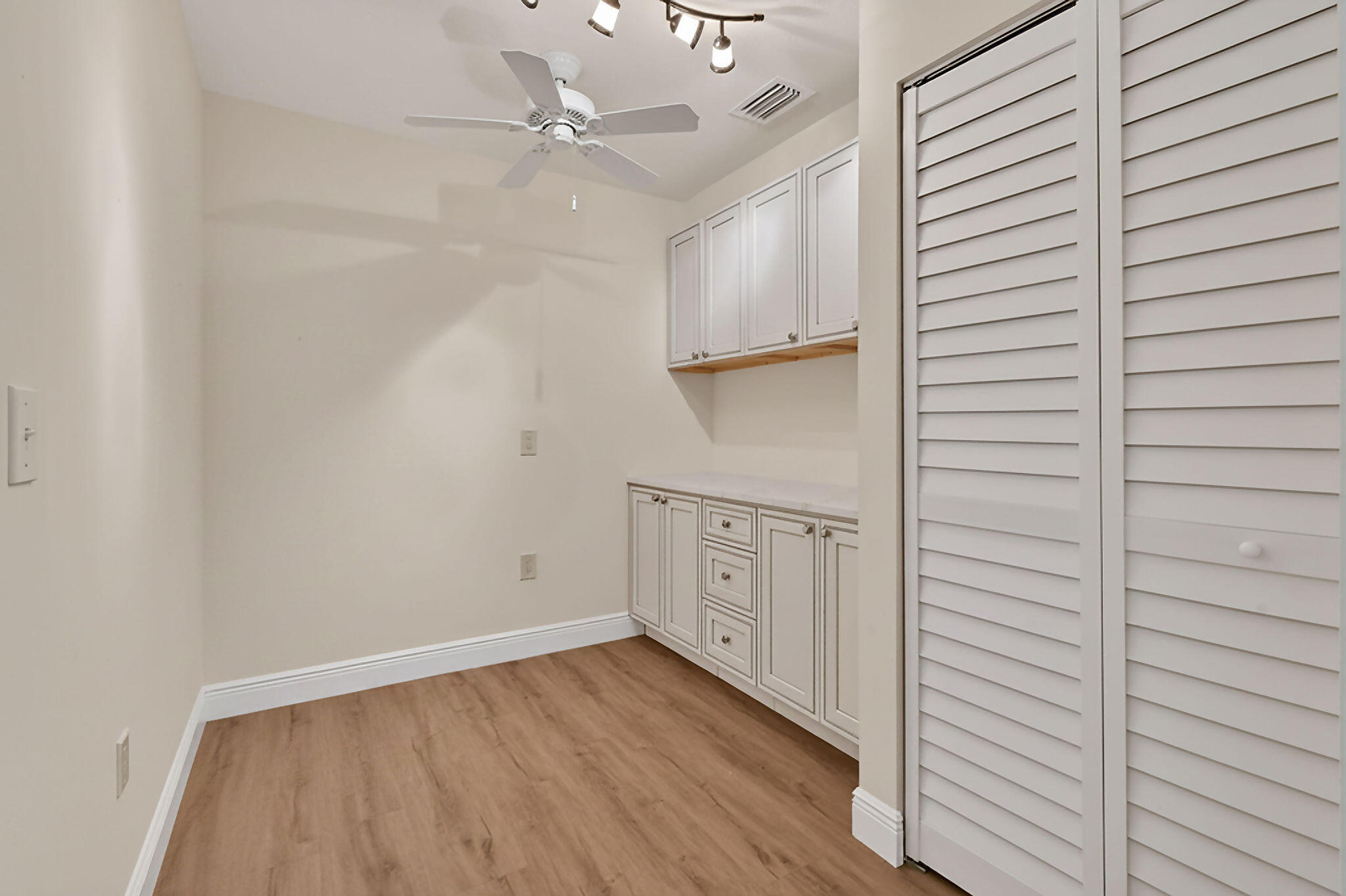 Empty room with built-in white cabinets, louvered closet doors, and wood-look flooring.