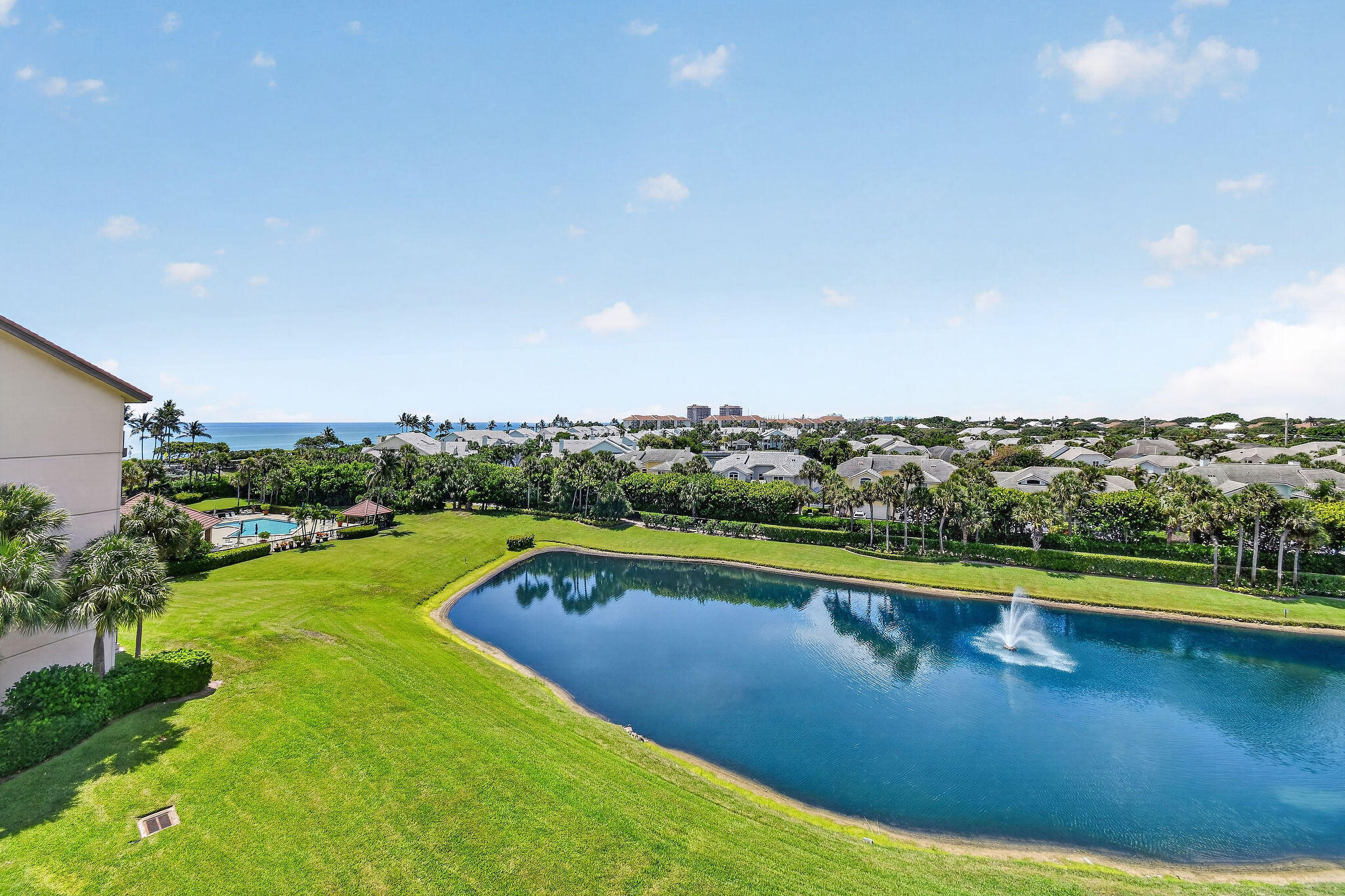 Aerial view of a coastal community with a fountain pond, swimming pool, and ocean beyond.