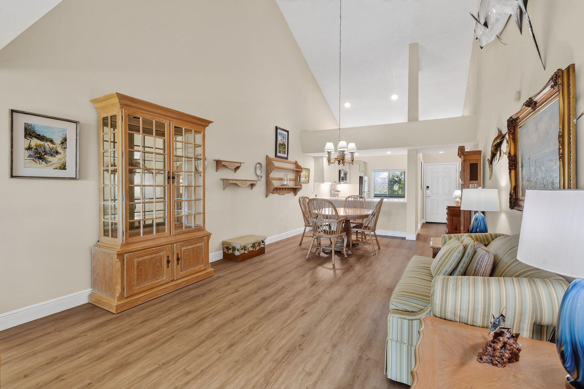 Open-plan living and dining area with vaulted ceiling, striped sofa, and wood-look flooring.