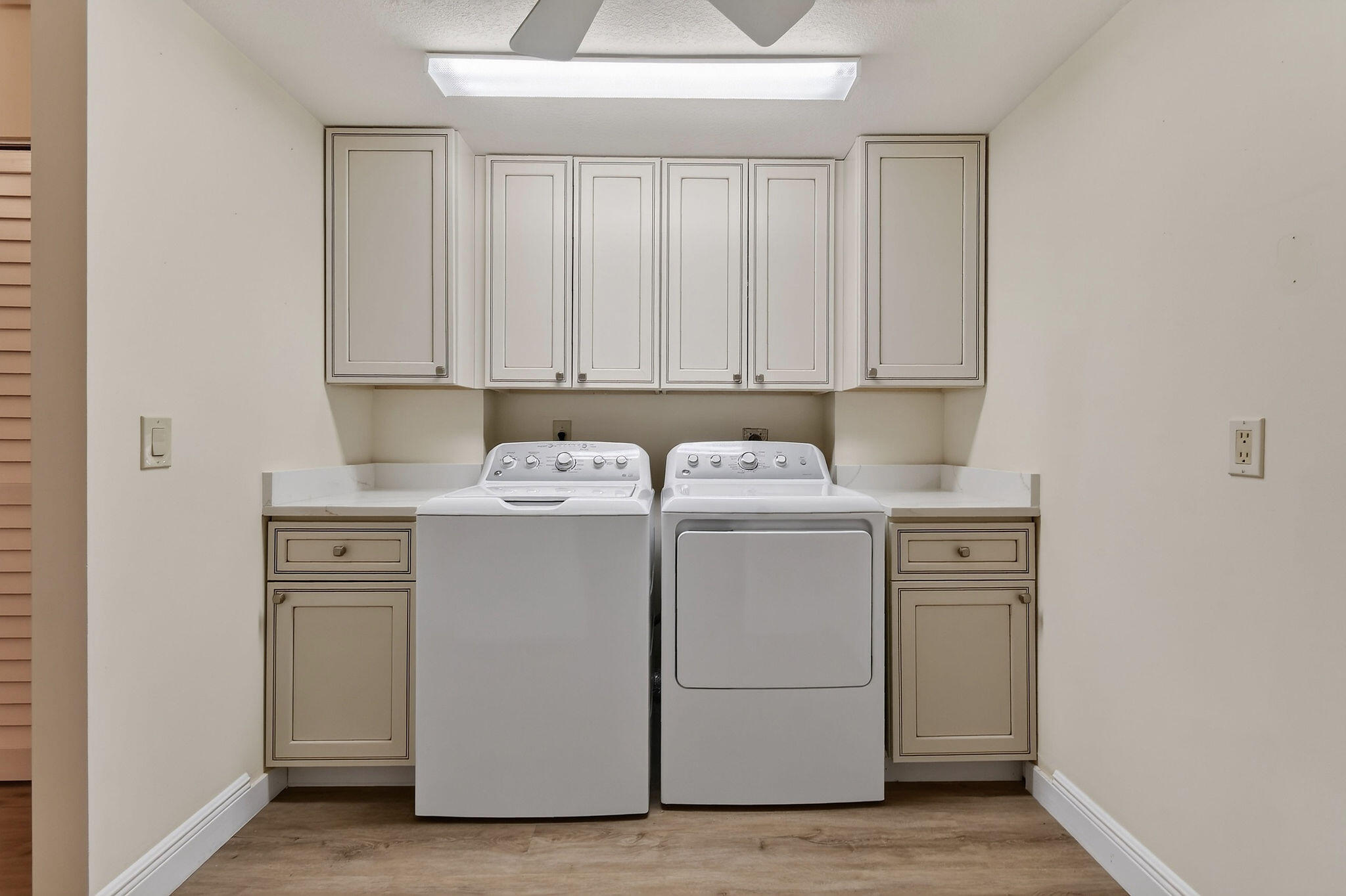 Laundry room with a washer and dryer beneath beige cabinets and countertops.
