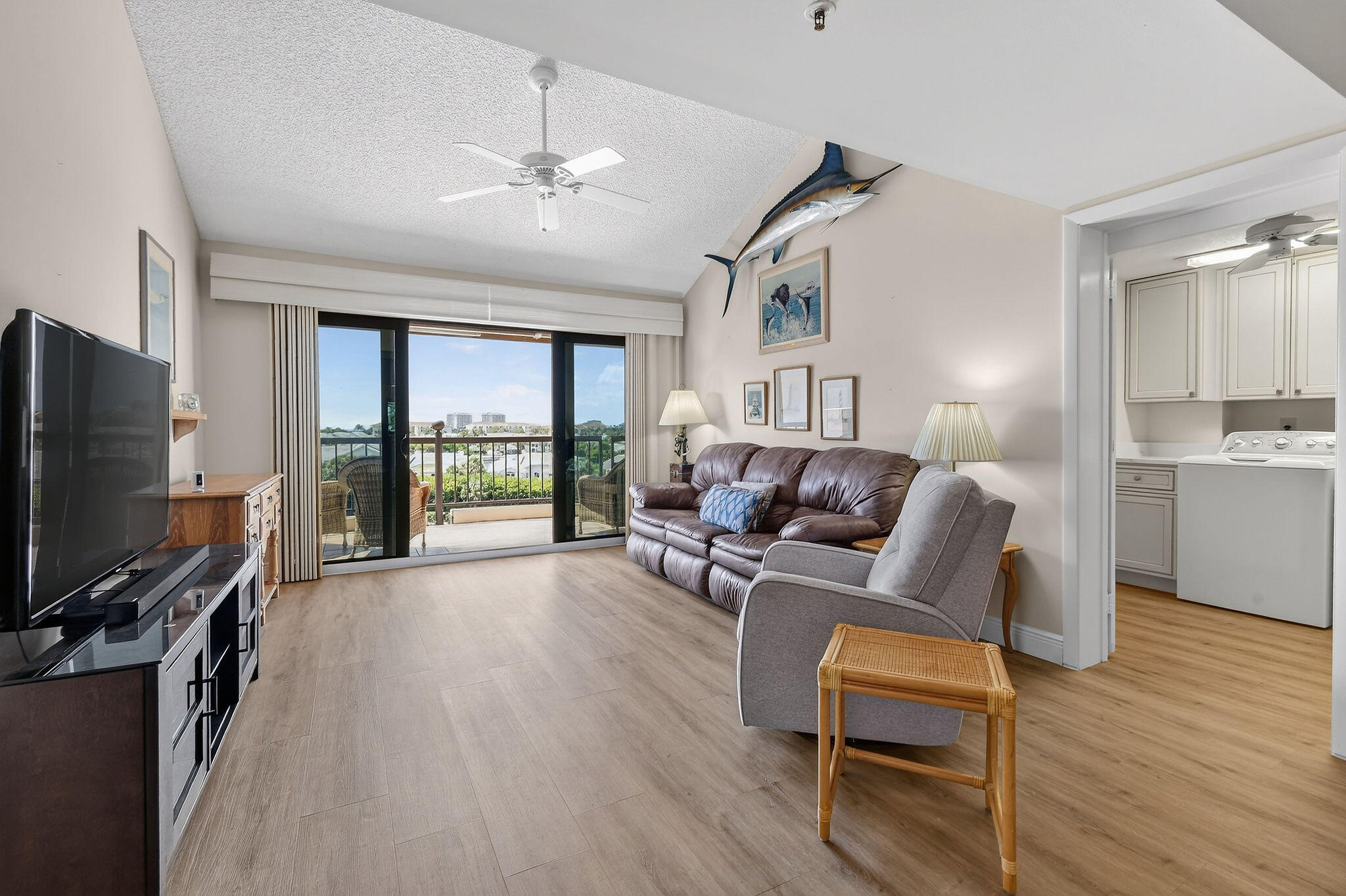 Living room with a leather sofa, gray armchair, and balcony access through sliding glass doors.