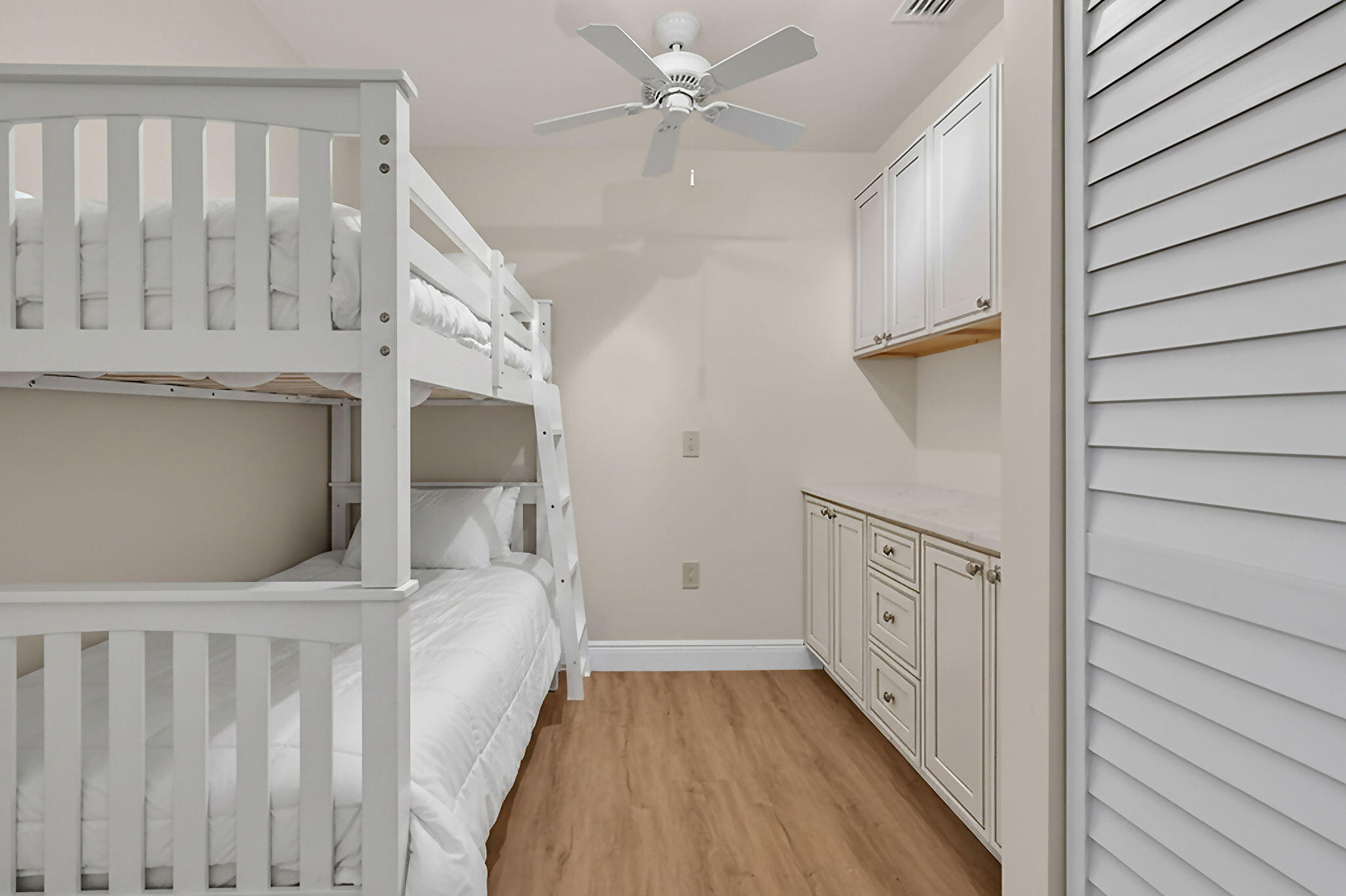 Bedroom with a white bunk bed beside built-in cabinets and wood-look flooring.