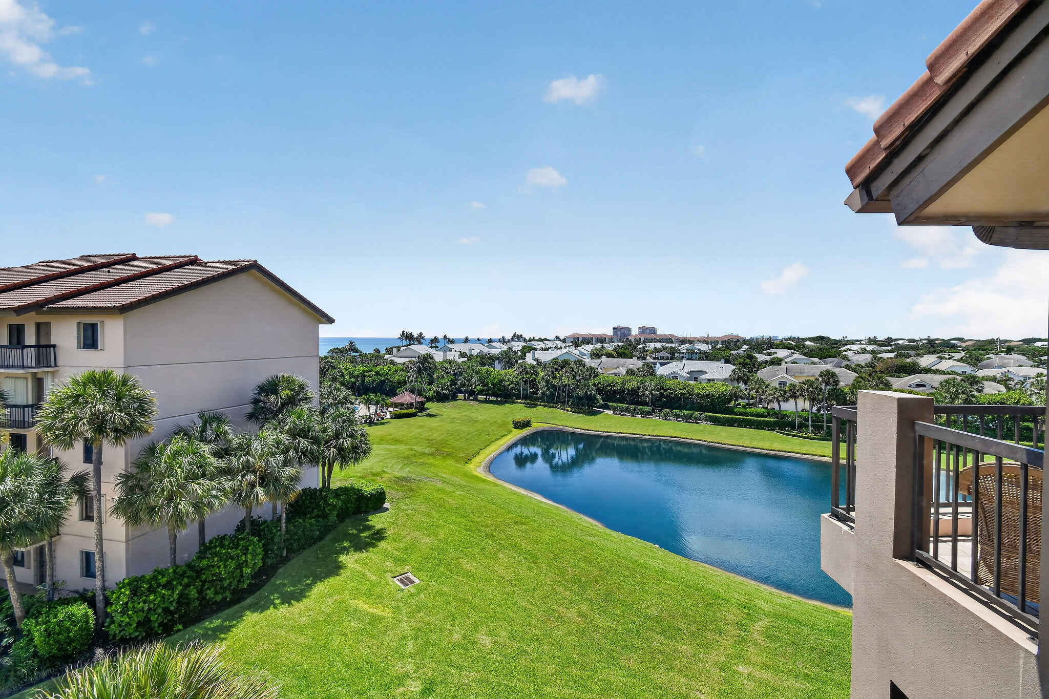 Balcony view of a landscaped community pond, palm trees, and the ocean on the horizon.