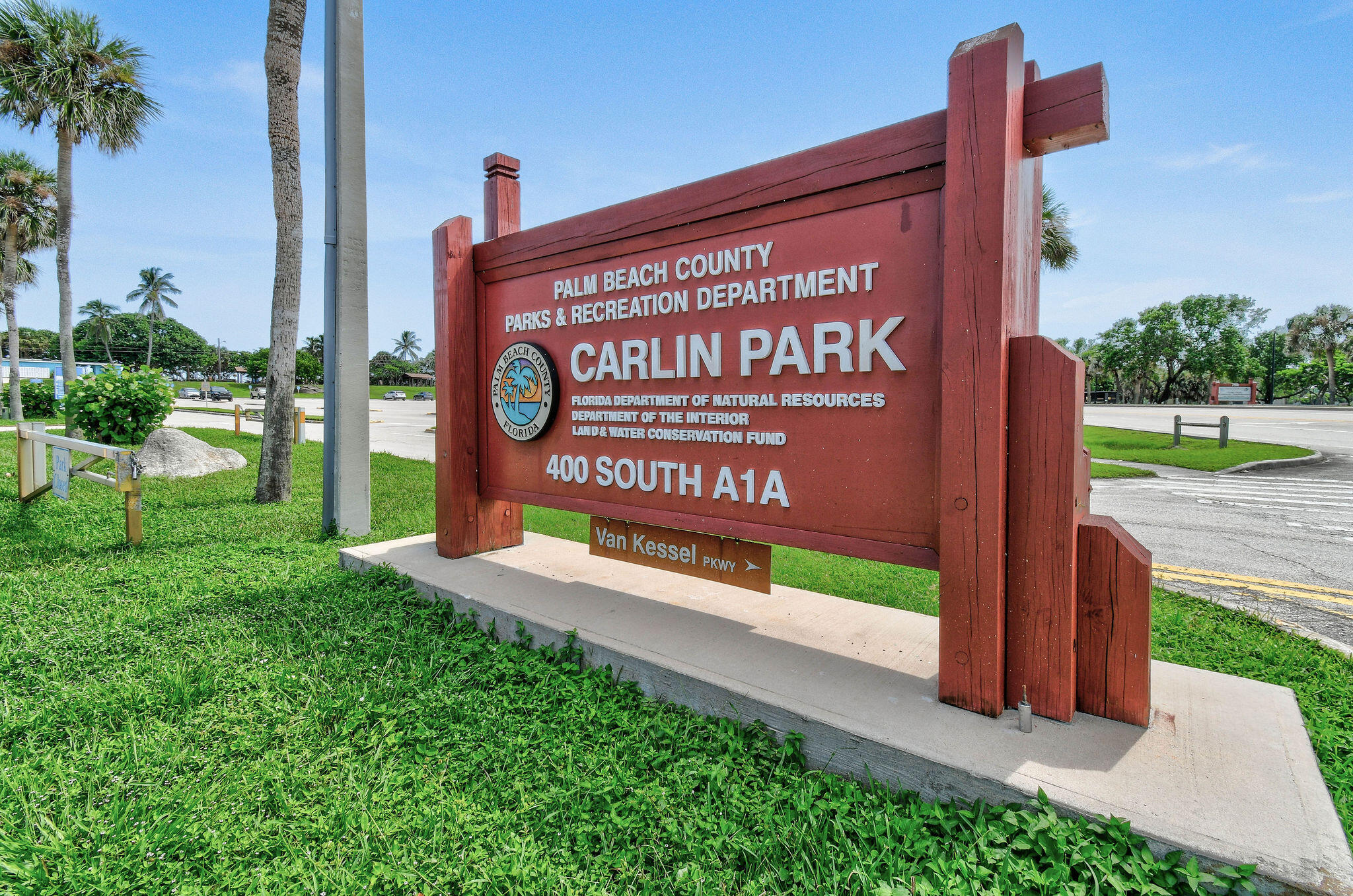 Carlin Park entrance sign beside a palm-lined road in Jupiter, Florida.
