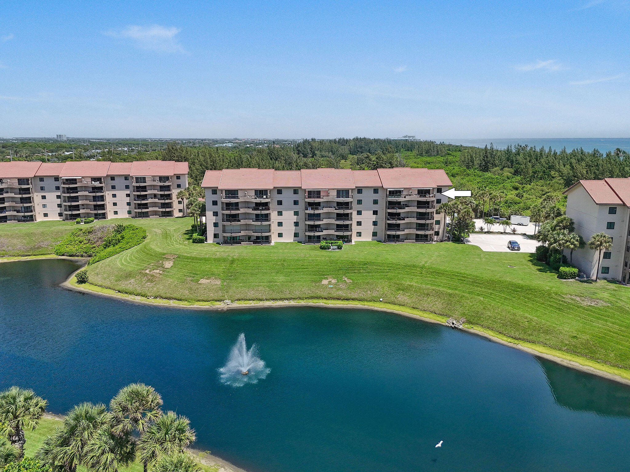 Aerial view of condominiums beside a lagoon, with an arrow pointing to a unit and ocean on the horizon.