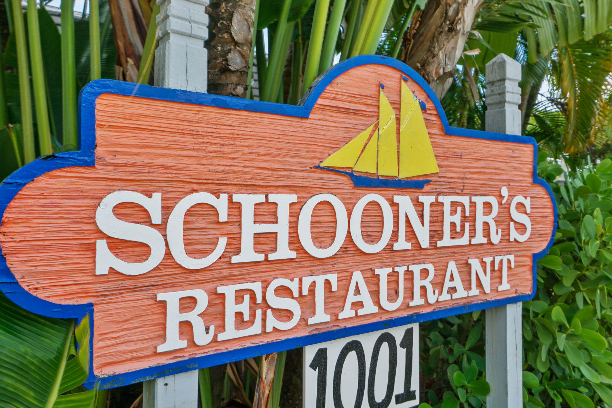 Schooner’s Restaurant sign with a yellow sailboat emblem and tropical foliage.