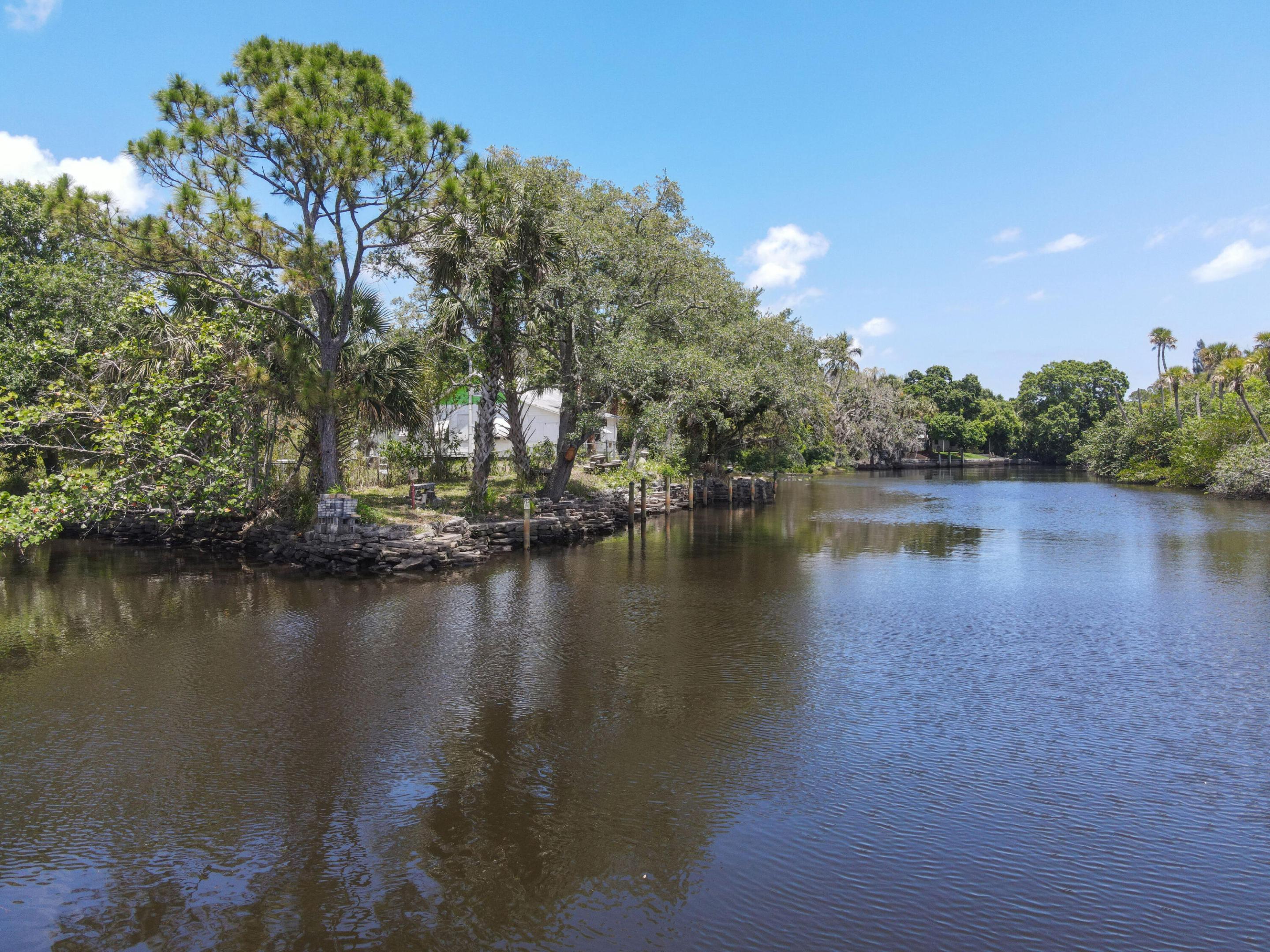 Canal-side property with a stone seawall, small dock, and mature trees.