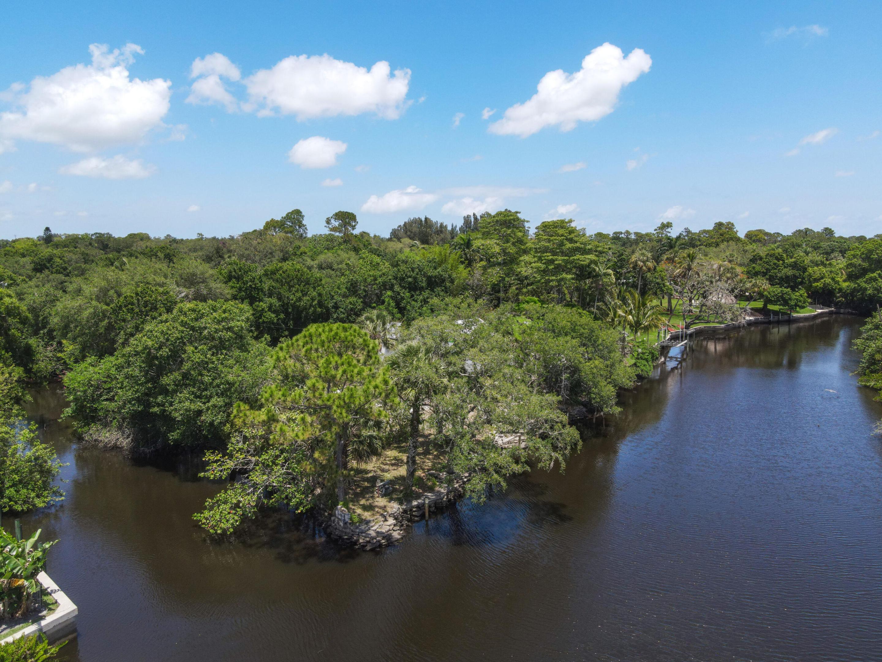 Aerial view of a wooded point surrounded by water, with a dock along the far shoreline.