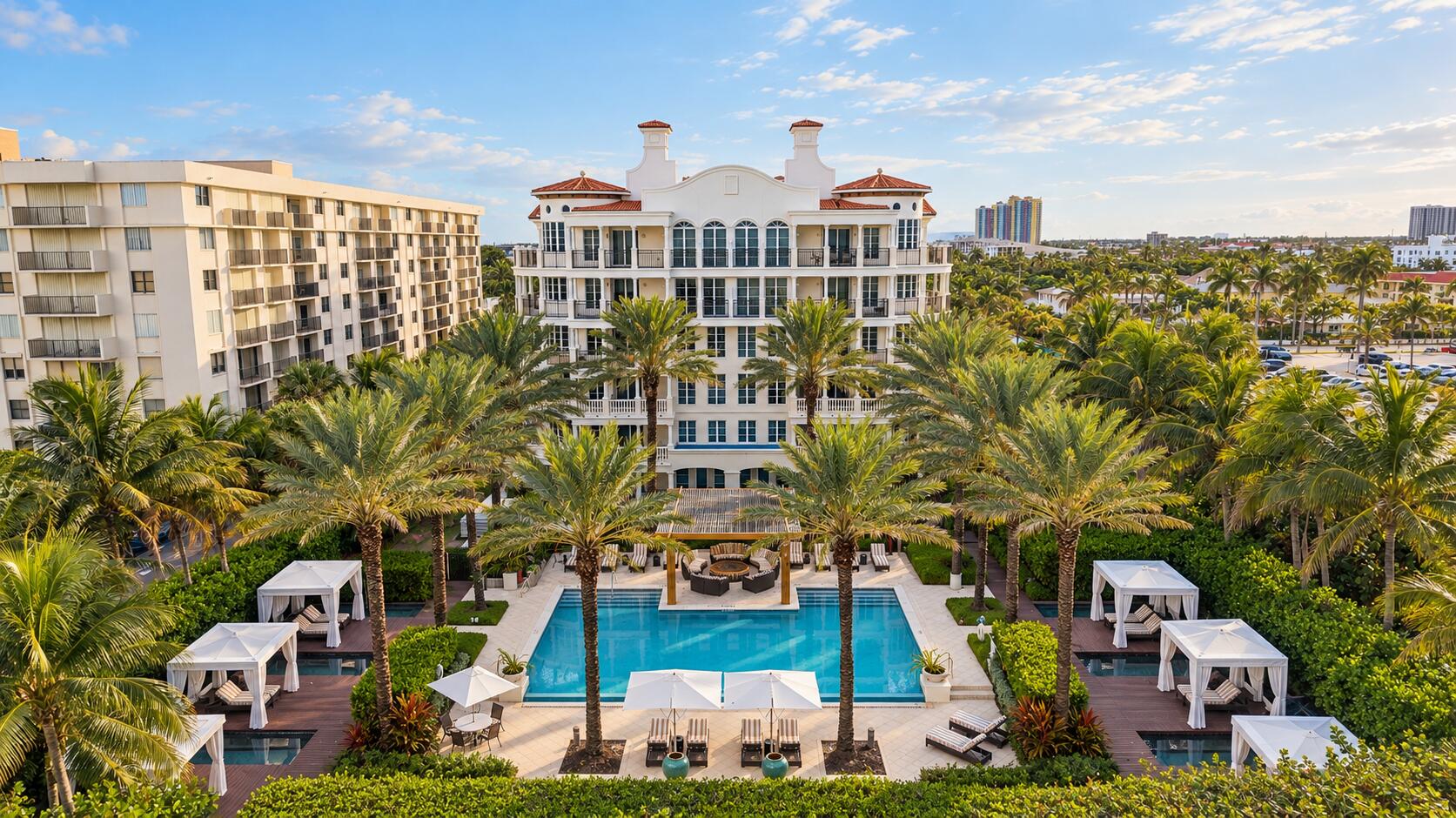 Aerial view of a palm-lined condominium courtyard with a central pool and cabanas.