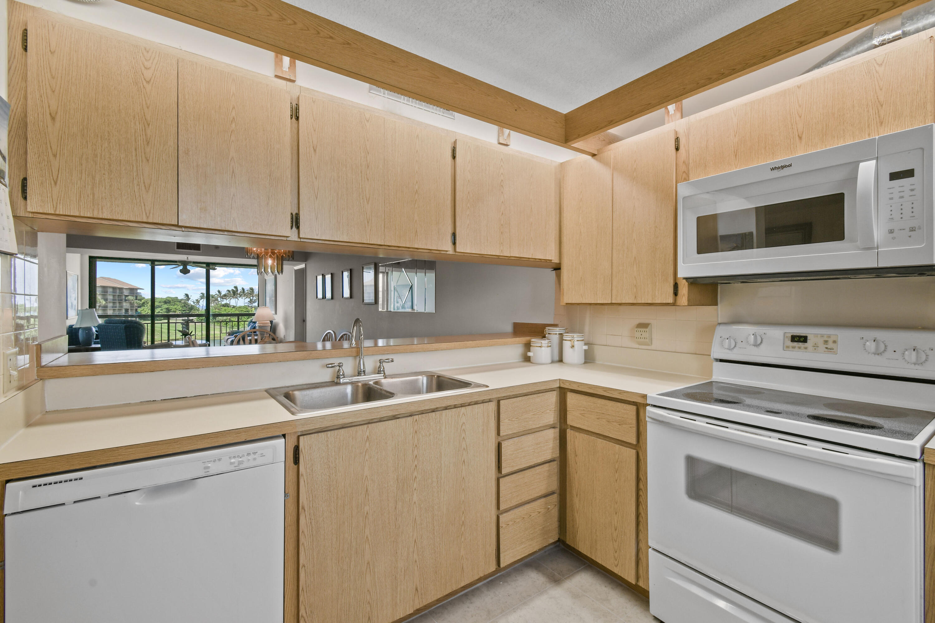 Kitchen with light wood cabinets, a double-basin sink, white appliances, and a pass-through to the living area.
